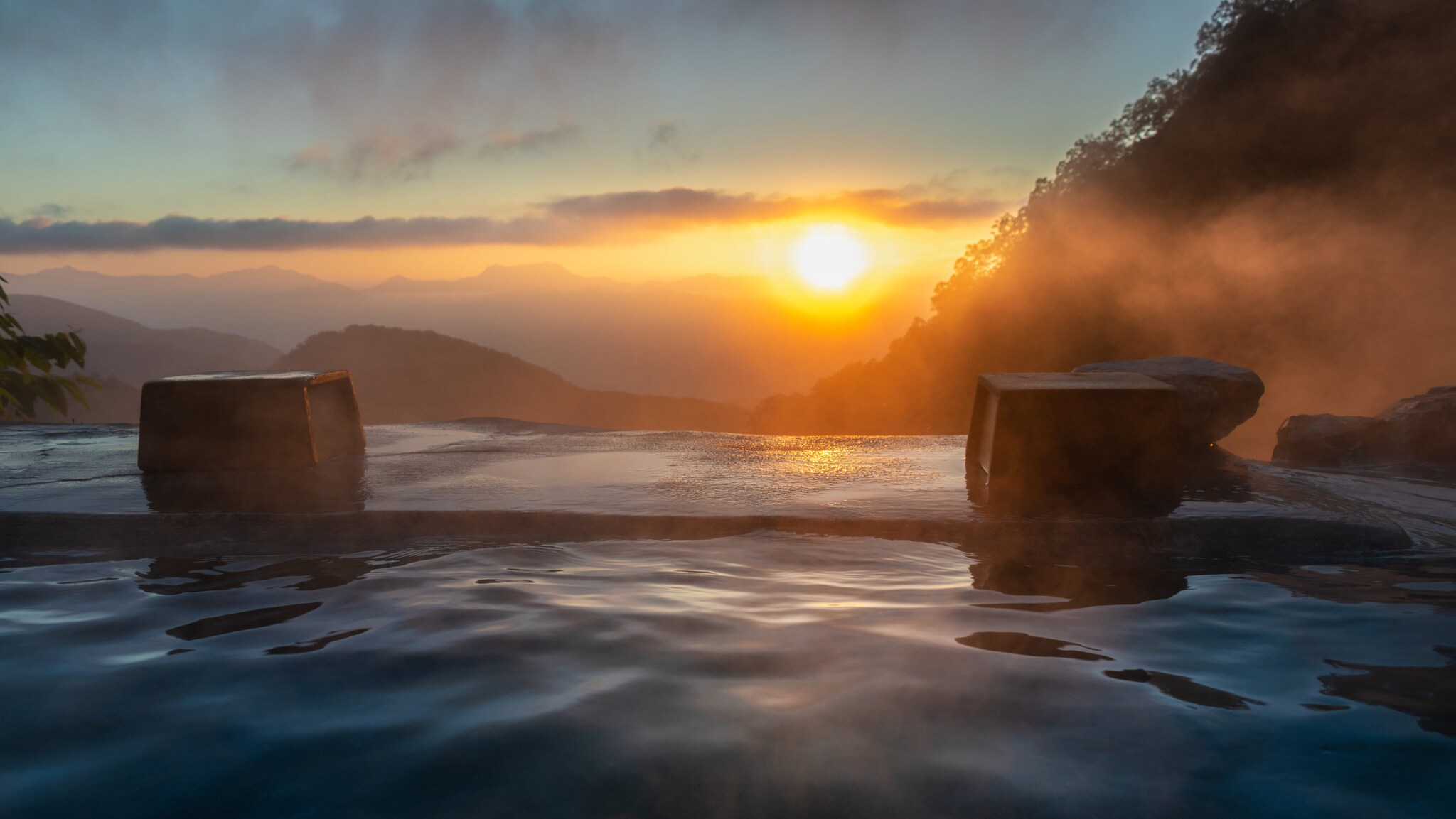 Sonnenuntergang über nebligen Bergen mit Blick auf einen Infinity-Pool im Vordergrund