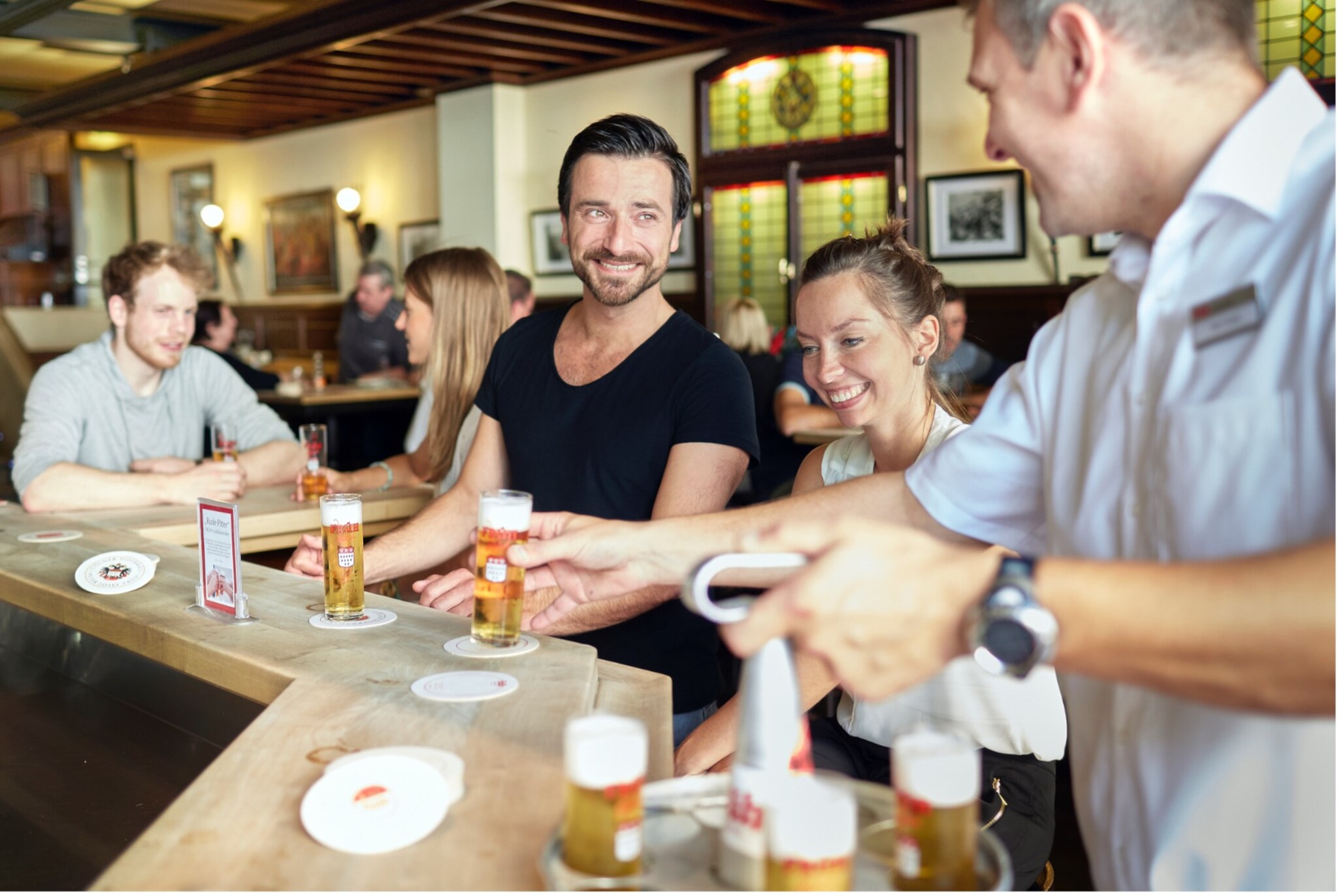 Mehrere Personen sitzen an einer Bar im Früh Brauhaus und erhalten Gläser mit Kölsch-Bier vom Kellner.