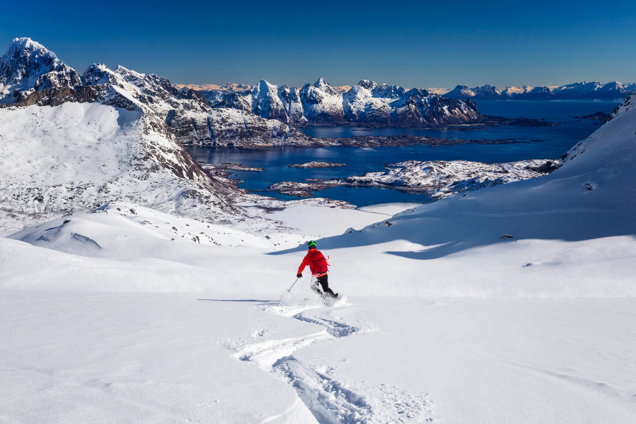 Ein Skifahrer in einer roten Jacke fährt durch den Schnee, im Hintergrund sind Berge.