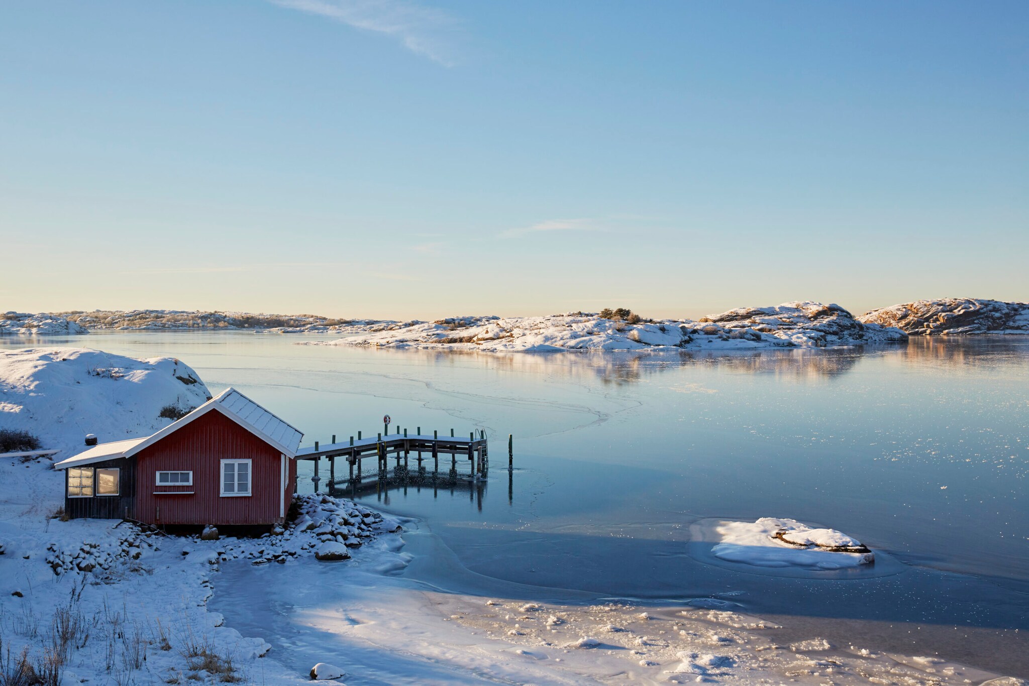 Rote schwedische Hütte, die in einer Winterlandschaft am See steht.