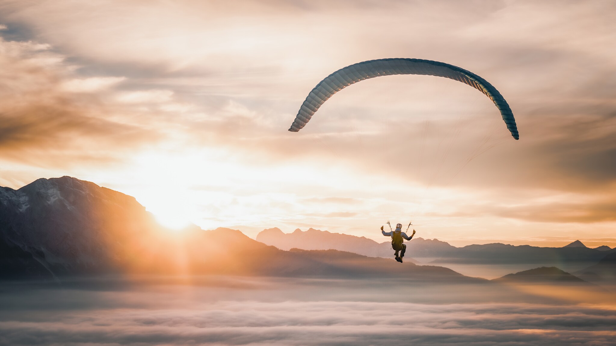 Person beim Gleitschirmfliegen über neblige Berglandschaft bei Sonnenaufgang Person beim Gleitschirmfliegen über neblige Berglandschaft bei Sonnenaufgang