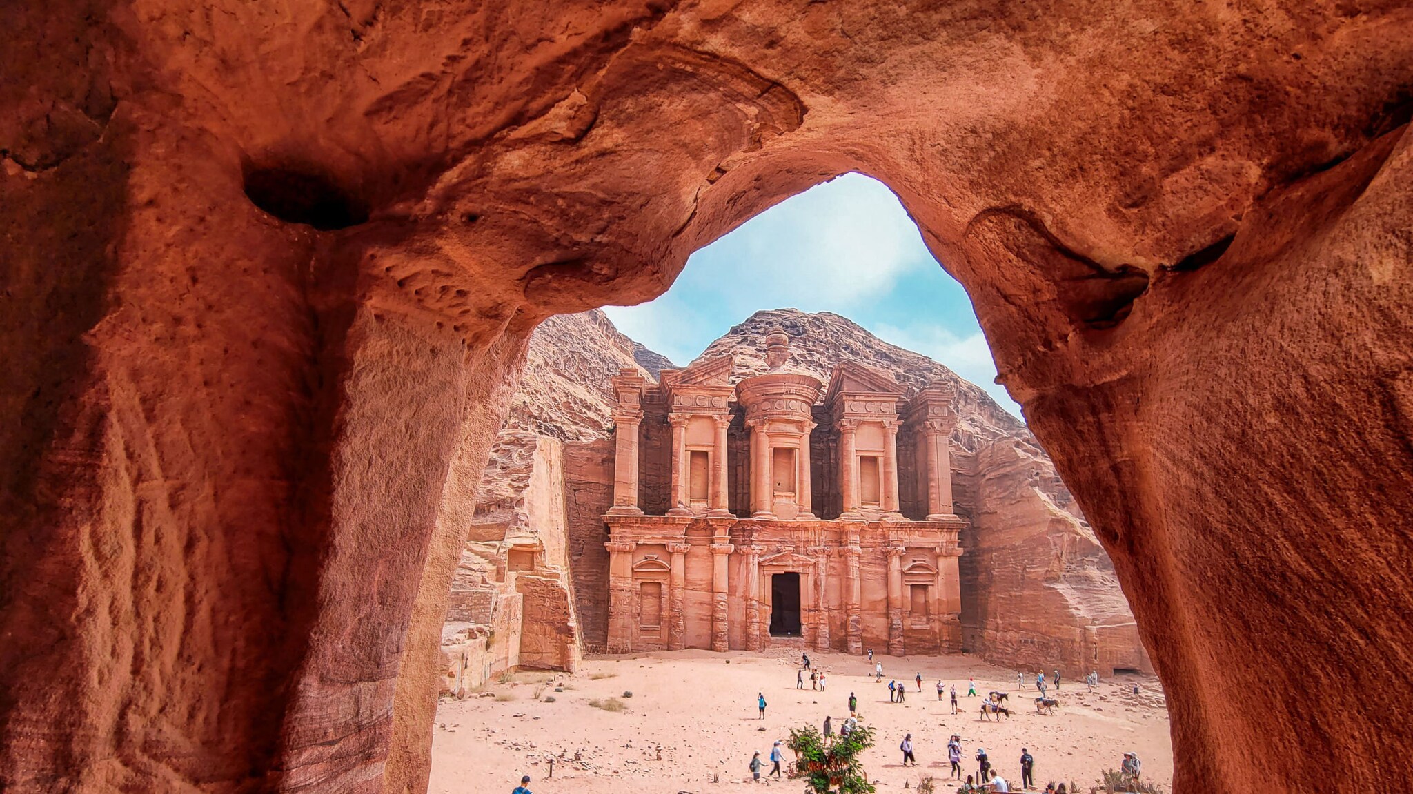 Blick durch eine Felsöffnung auf das antike Kloster Monastery in Petra, Jordanien, mit Touristen im Vordergrund
