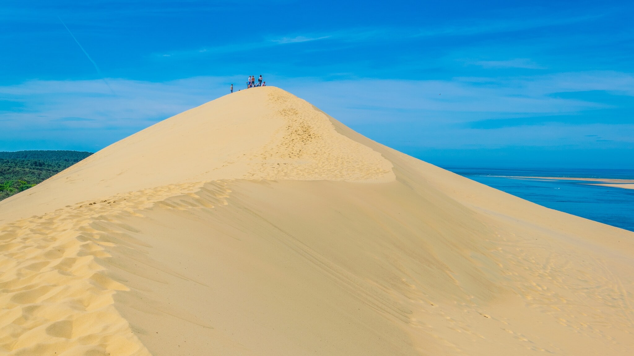 Menschen stehen auf der Spitze einer großen Sanddüne unter blauem Himmel Menschen stehen auf der Spitze einer großen Sanddüne unter blauem Himmel