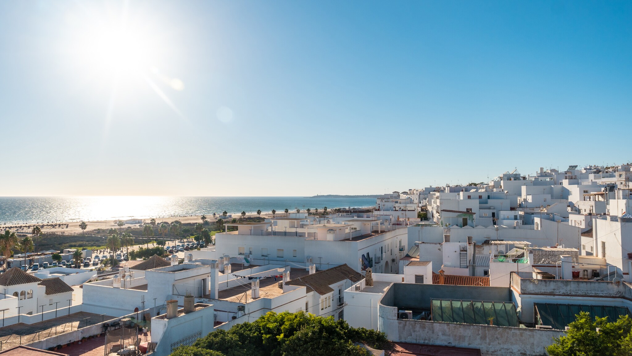 Blick auf weiße Häuser einer Küstenstadt bei klarem Himmel und Sonne über dem Meer