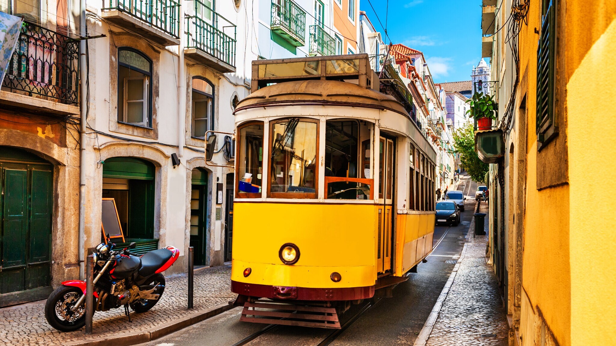 Gelbe historische Straßenbahn fährt durch enge Gasse mit mehrstöckigen Häusern in Lissabon