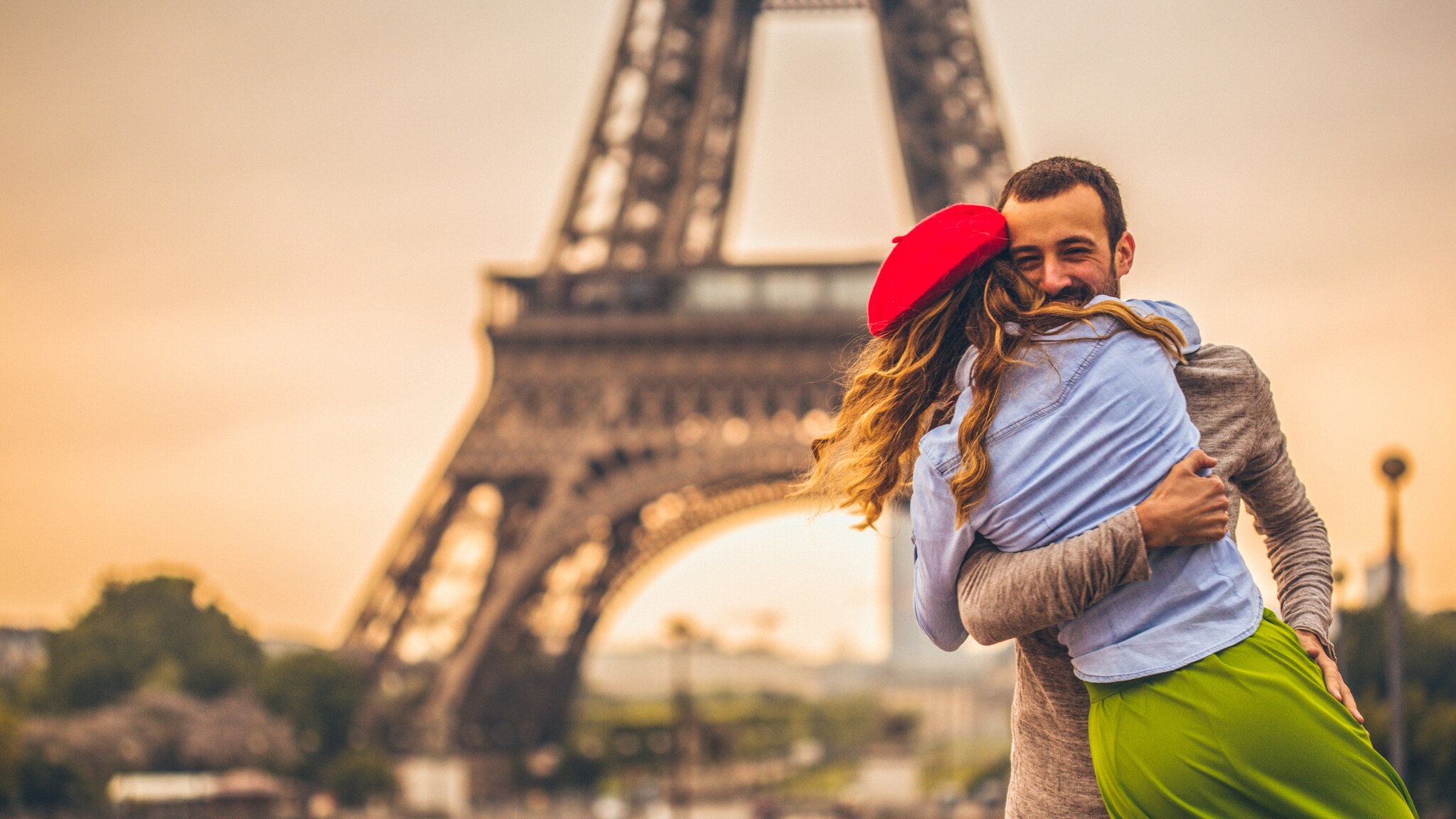 Paar umarmt sich glücklich vor dem Eiffelturm bei Sonnenuntergang in Paris