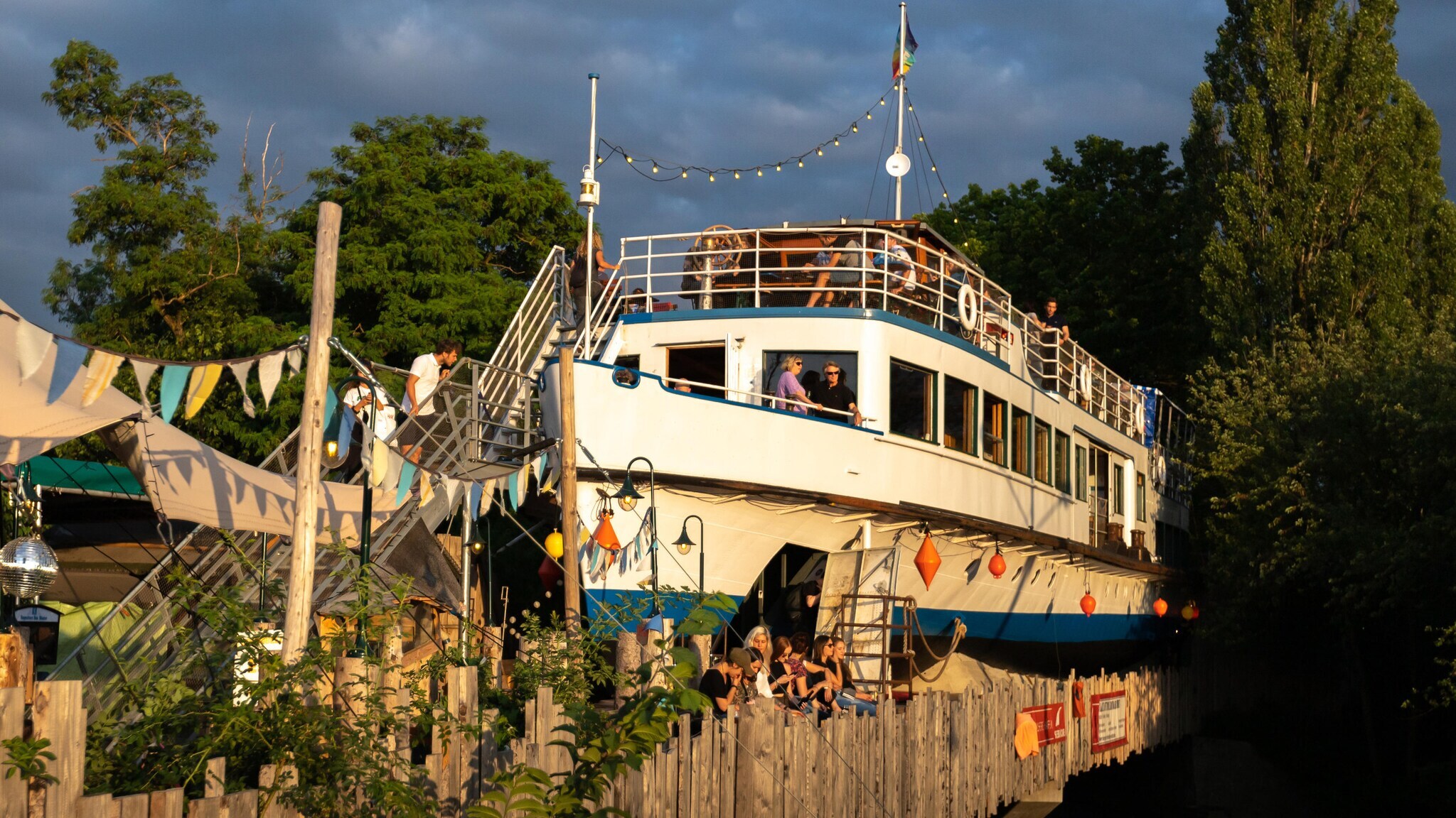 Alte Utting, ein stillgelegtes Passagierschiff auf einer Brücke im Schlachthofviertel München, mit Menschen an Deck und Dekoration Alte Utting, ein stillgelegtes Passagierschiff auf einer Brücke im Schlachthofviertel München, mit Menschen an Deck und Dekoration