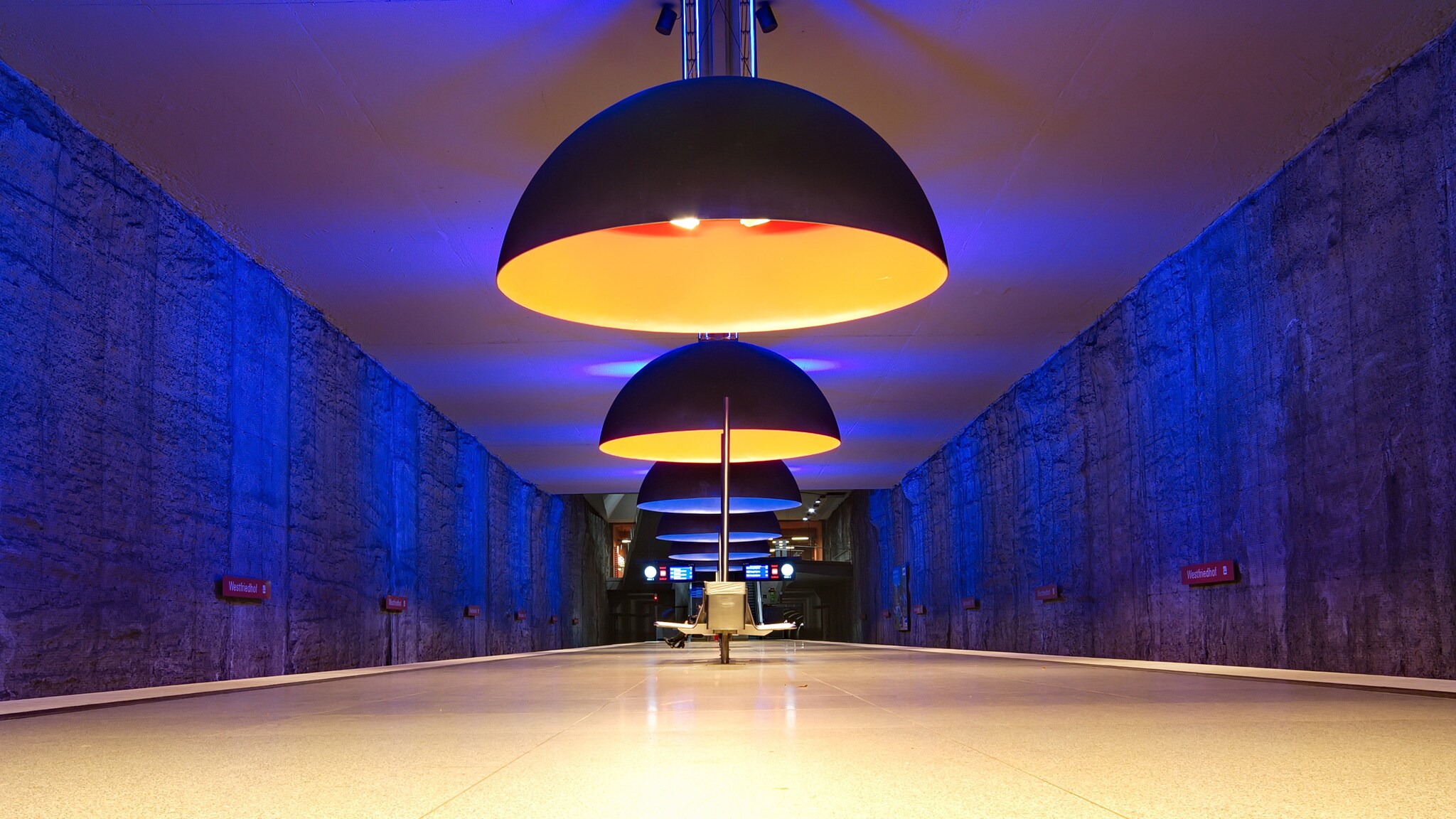 Drei große, runde Pendelleuchten hängen über einem langen, leeren Flur mit blauen Wänden