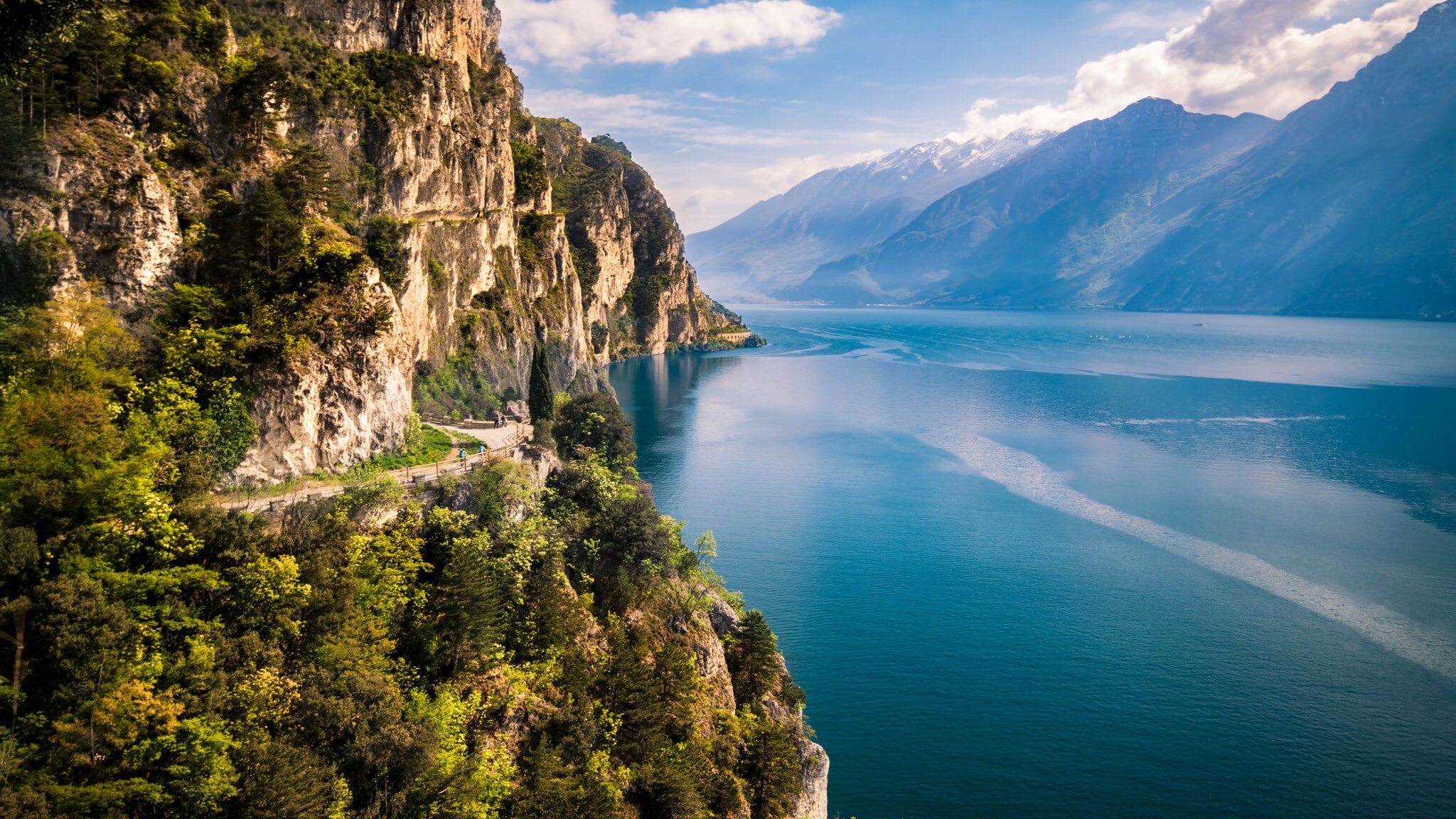Bewachsene Felswand nahe Riva del Garda direkt am Gardasee mit Gipfeln auf der anderen Seeseite im Hintergrund. Bewachsene Felswand nahe Riva del Garda direkt am Gardasee mit Gipfeln auf der anderen Seeseite im Hintergrund.