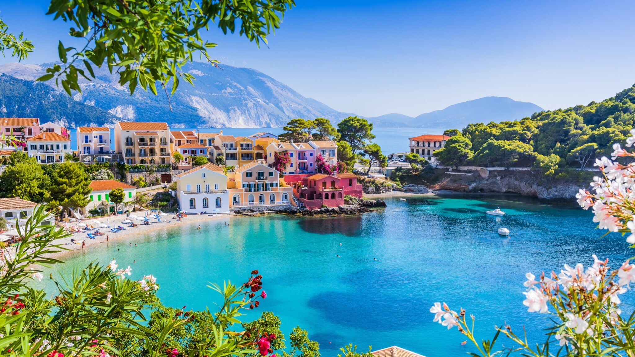 Bunte Häuser am Ufer einer ruhigen Bucht mit türkisfarbenem Wasser, umgeben von grünen Hügeln und Bergen im Hintergrund