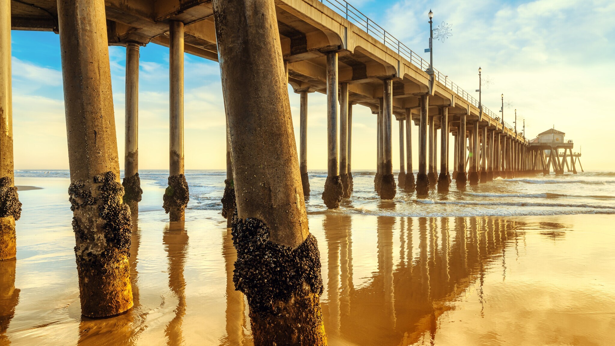 Blick unter einen langen Holzsteg mit Pfeilern im Wasser bei Sonnenuntergang am Strand