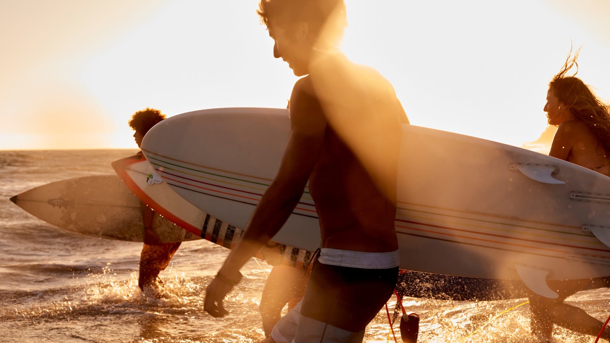 Drei Surfer mit Surfboards laufen bei Sonnenuntergang ins Wasser am Strand Drei Surfer mit Surfboards laufen bei Sonnenuntergang ins Wasser am Strand