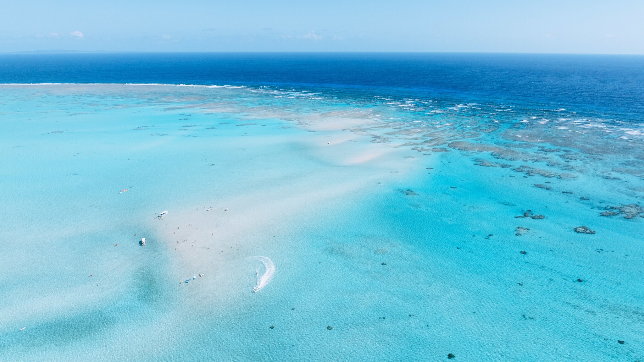 Luftaufnahme einer weißen Sandbank mit Booten und Personen im türkisblauen Meer.