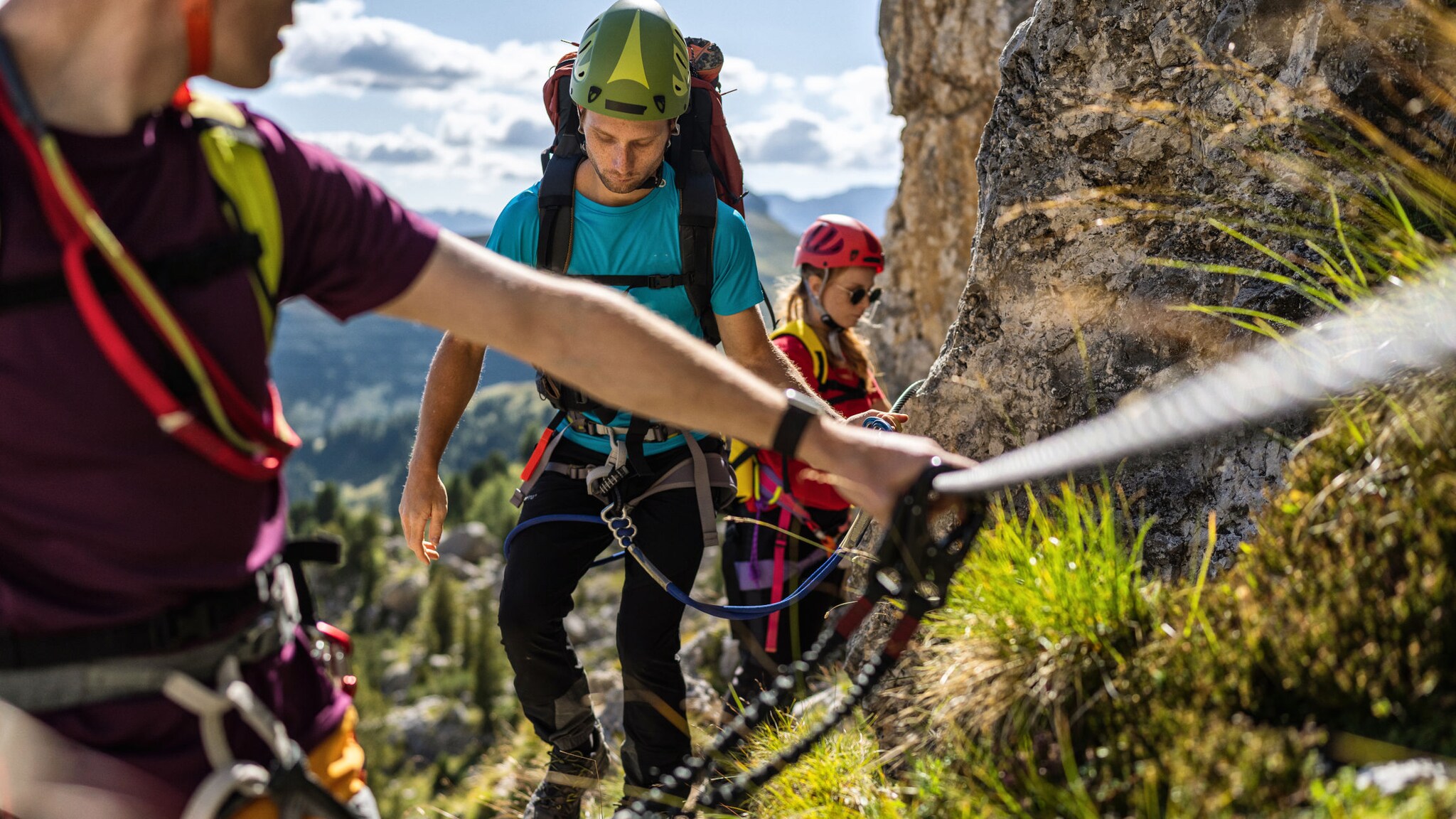 Drei Personen in Kletterausrüstung an einem Felsen mit Drahtseil.