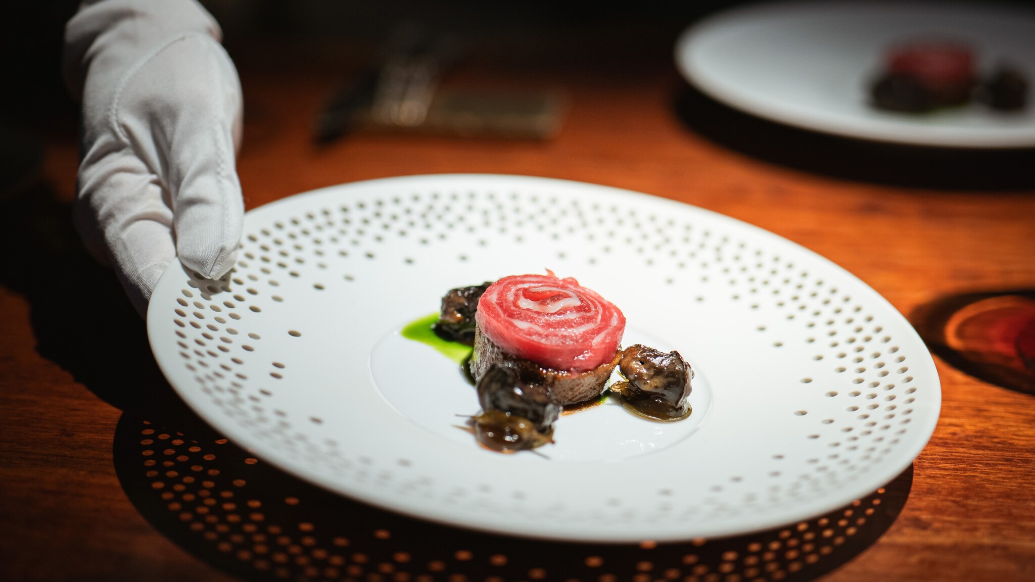 Hand mit weißem Handschuh serviert Teller mit kunstvoll angerichtetem Gericht