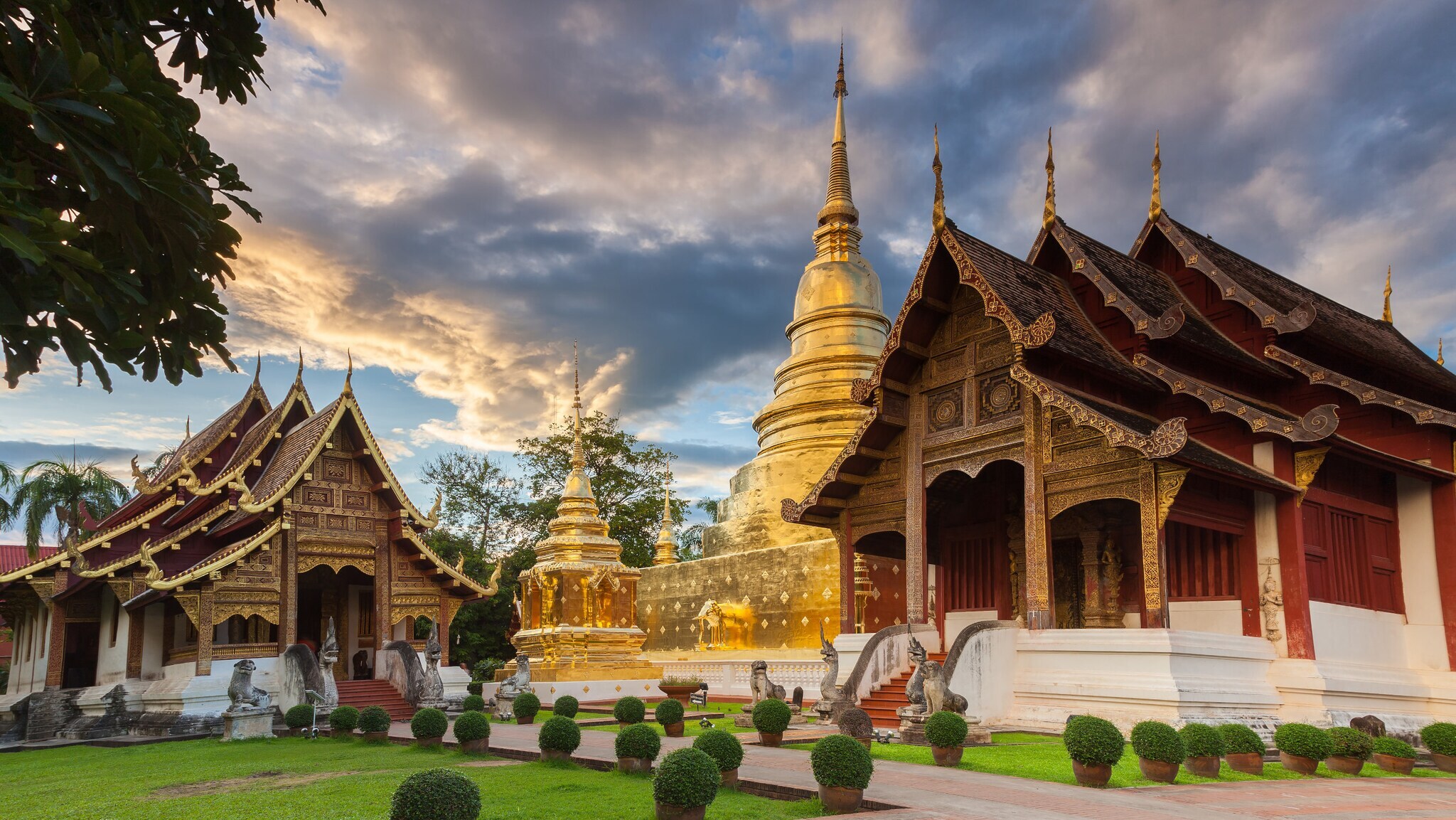 Goldene Pagode und traditionelle thailändische Tempelgebäude mit verzierten Dächern bei Sonnenuntergang in Chiang Mai, Thailand