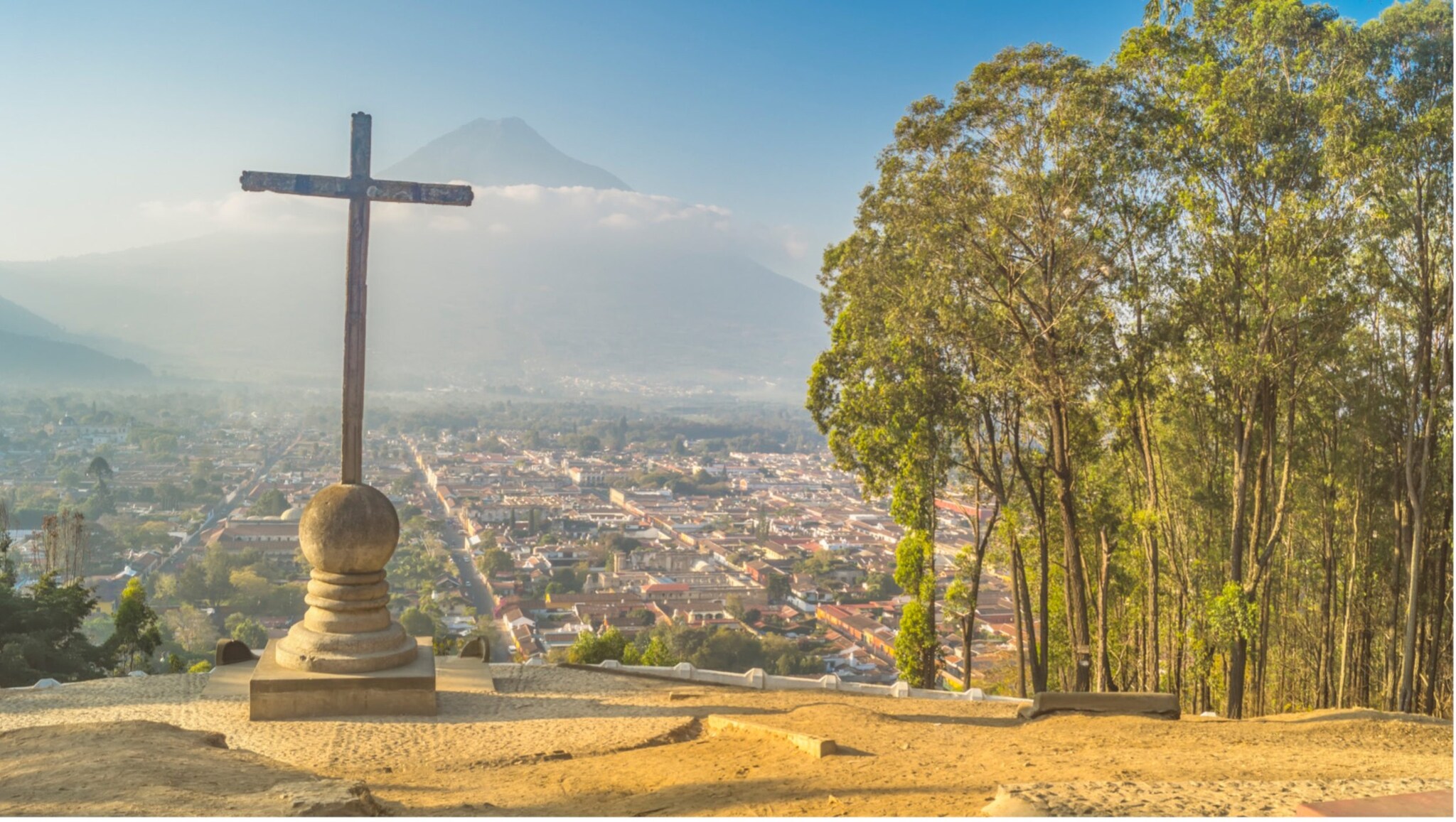 Holzkreuz auf einem Hügel mit Blick auf eine Stadt und einen Berg im Hintergrund