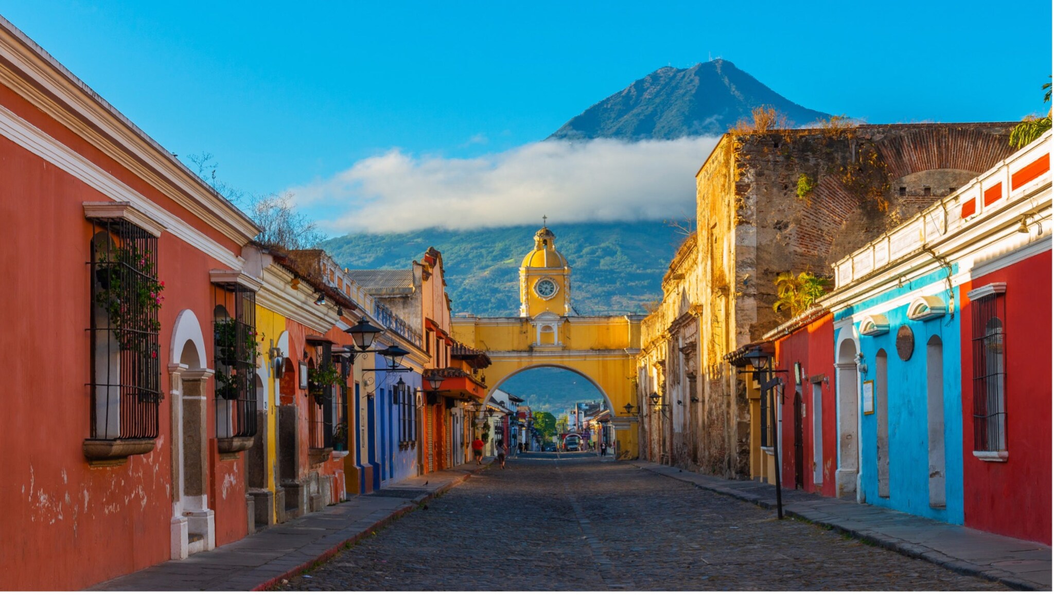 Blick auf die gelbe Santa-Catalina-Arkade in Antigua, Guatemala, mit Kopfsteinpflasterstraße und Vulkan Agua im Hintergrund Blick auf die gelbe Santa-Catalina-Arkade in Antigua, Guatemala, mit Kopfsteinpflasterstraße und Vulkan Agua im Hintergrund