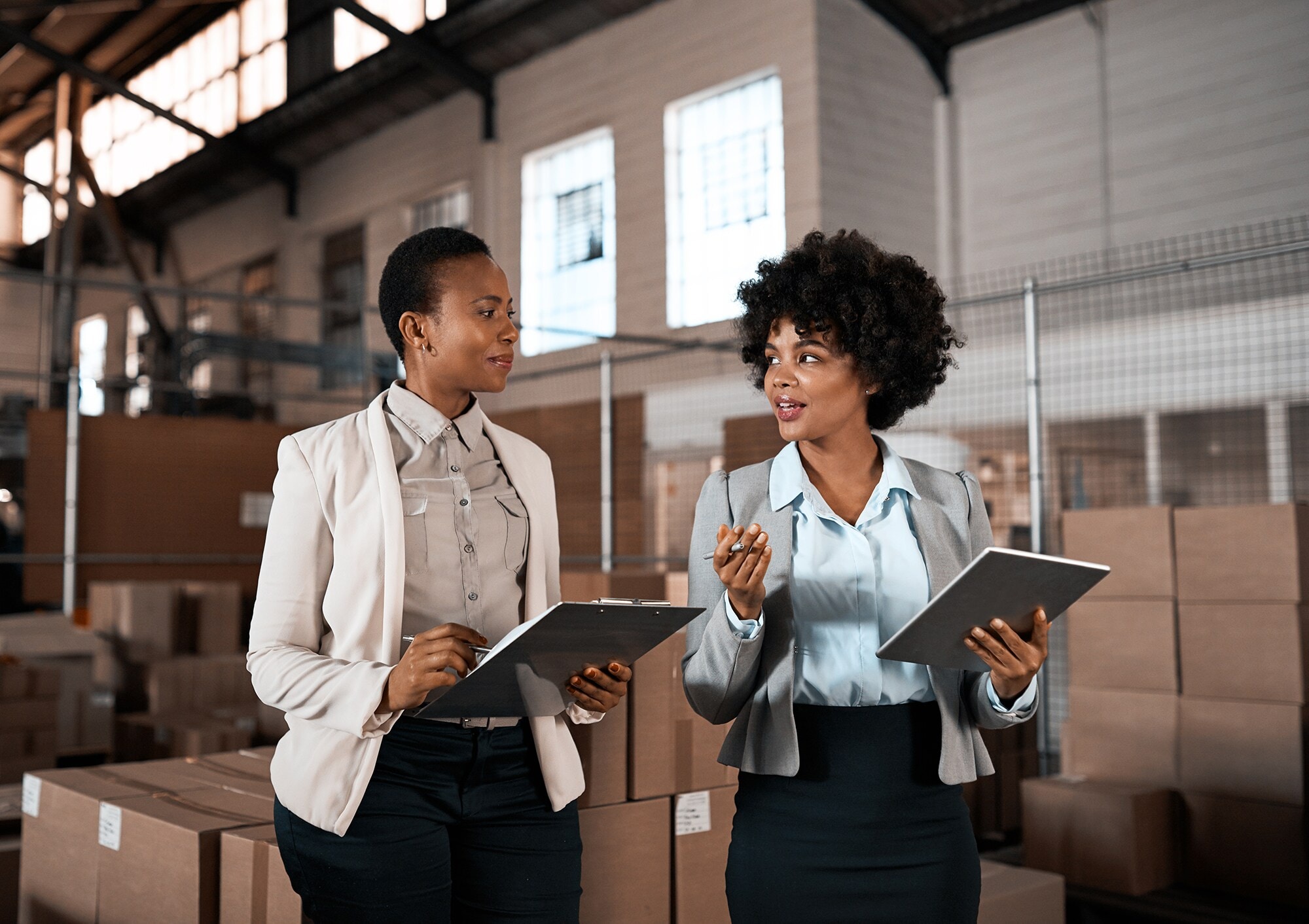 Female Leadership: So profitieren Unternehmen von Frauen in Führungspositionen Zwei erfolgreiche weibliche Führungskräfte besprechen sich im Logistikzentrum.