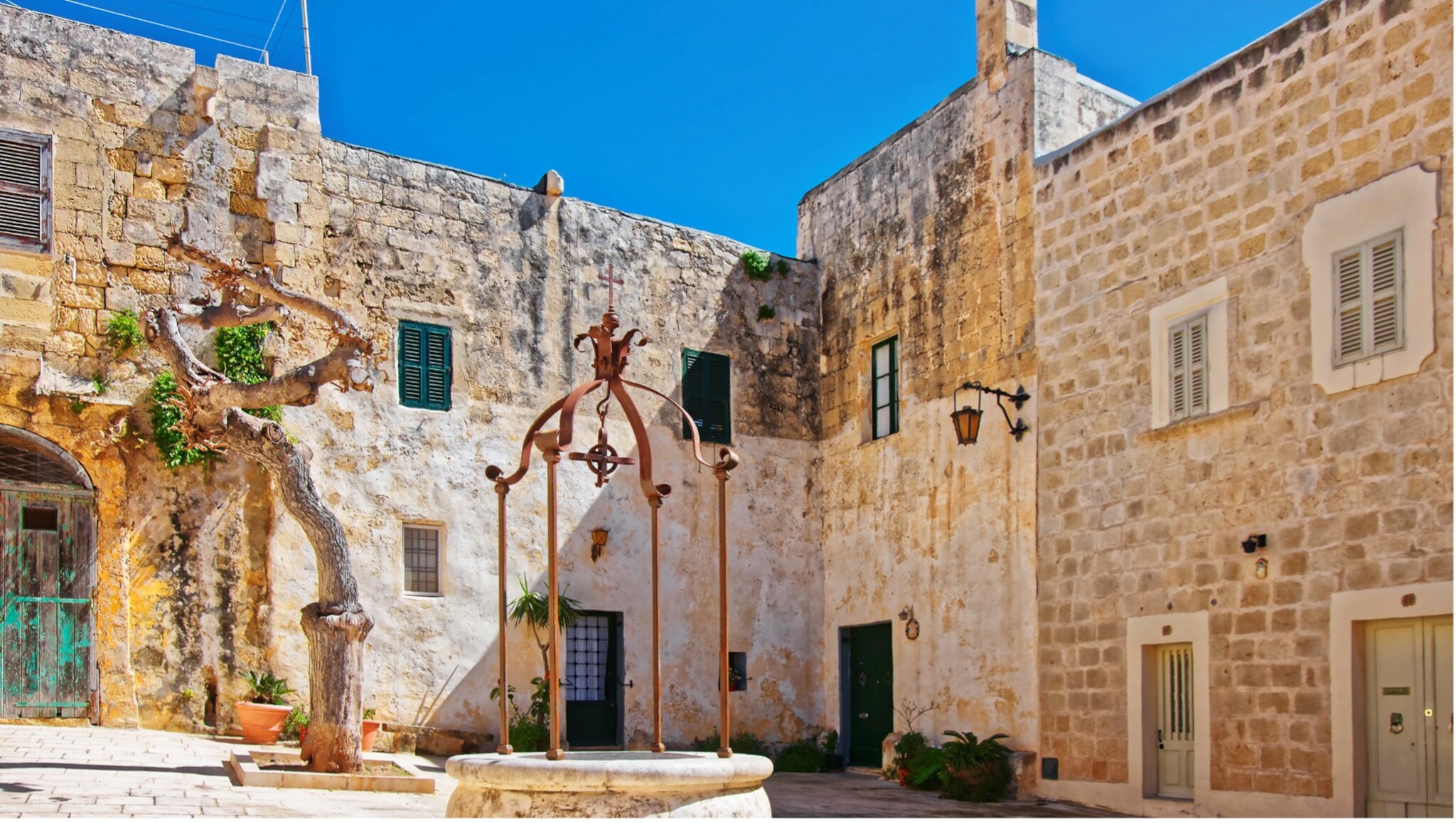 Innenhof eines historischen Steinhauses mit einem alten Brunnen in der Mitte und blauem Himmel