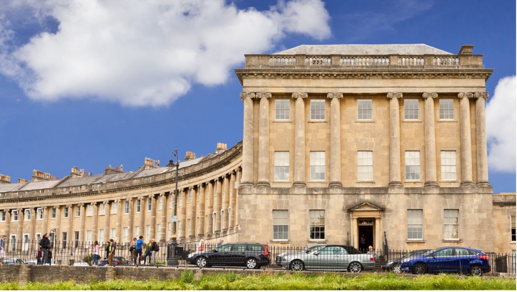 Historisches Gebäude mit Säulen und vielen Fenstern, davor parkende Autos und Menschen auf dem Bürgersteig Historisches Gebäude mit Säulen und vielen Fenstern, davor parkende Autos und Menschen auf dem Bürgersteig