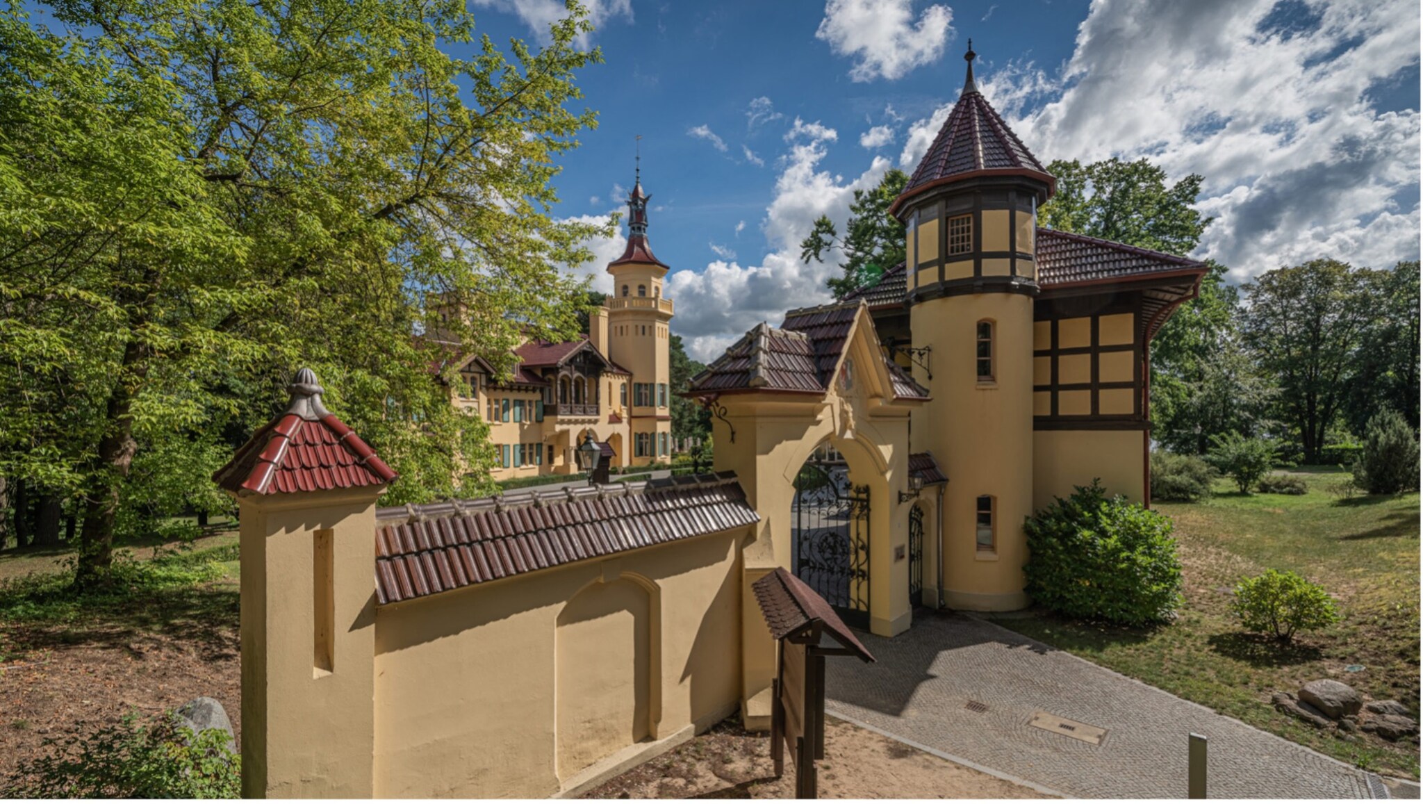 Eingangstor und Turm eines historischen Schlosses mit Fachwerk und gelben Wänden unter blauem Himmel mit Wolken