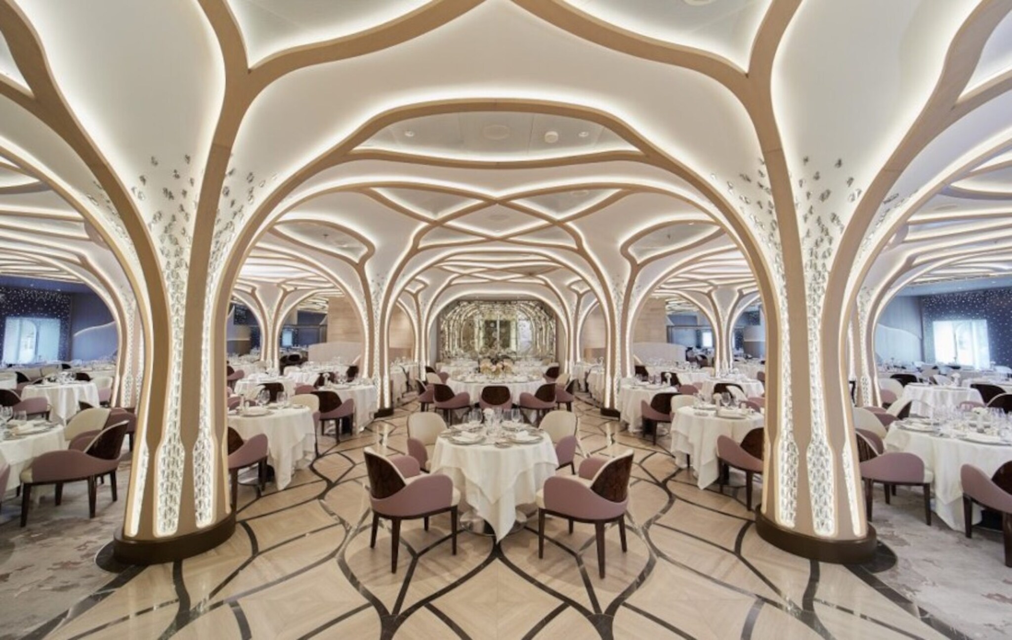 Eleganter, heller Speisesaal mit eingedeckten Tischen unter einer beleuchteten, geschwungenen Deckenkonstruktion in Form von weißen Baumkronen übergehend in Säulen als Baumstämmen.