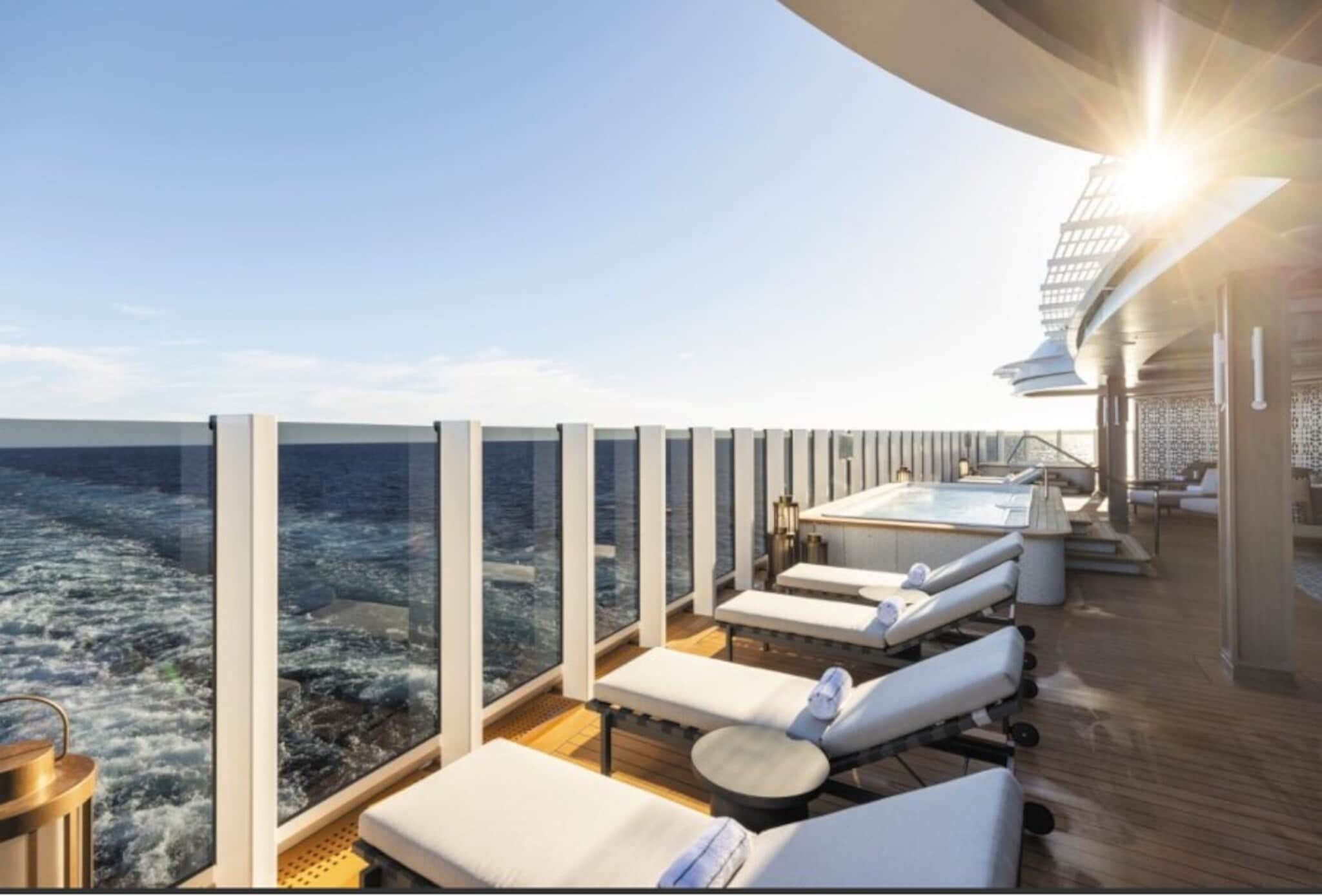 Gepolsterte Sonnenliegen auf einem Außendeck mit Whirlpool und Blick aufs offene Meer durch eine Reling aus Glas bei Sonnenschein. Gepolsterte Sonnenliegen auf einem Außendeck mit Whirlpool und Blick aufs offene Meer durch eine Reling aus Glas bei Sonnenschein.