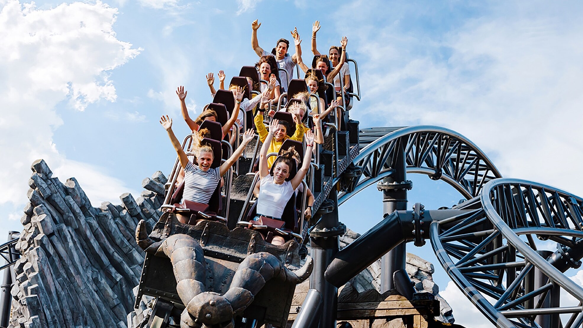 Menschen fahren auf der Achterbahn Taron im Phantasialand, Arme in die Luft gestreckt, vor blauem Himmel Menschen fahren auf der Achterbahn Taron im Phantasialand, Arme in die Luft gestreckt, vor blauem Himmel