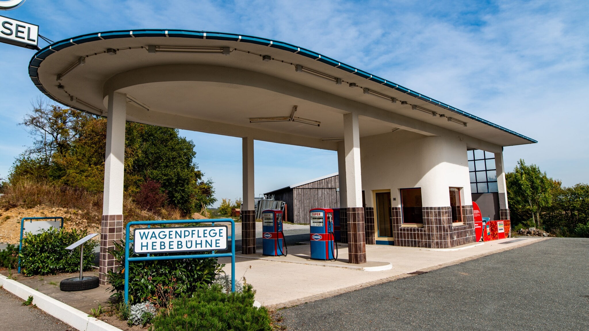 Tankstelle mit zwei Zapfsäulen unter einem großen, abgerundeten Dach, Schild mit den Worten Tankstelle mit zwei Zapfsäulen unter einem großen, abgerundeten Dach, Schild mit den Worten 'Wagenpflege Hebebühne'