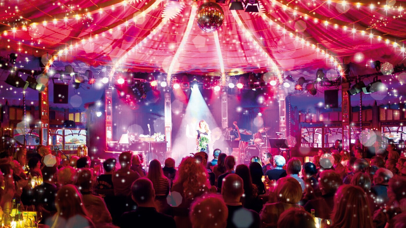 Bühne im Bar jeder Vernunft Theater Berlin mit Künstlerin im Scheinwerferlicht vor Publikum unter Zelt mit Lichterketten