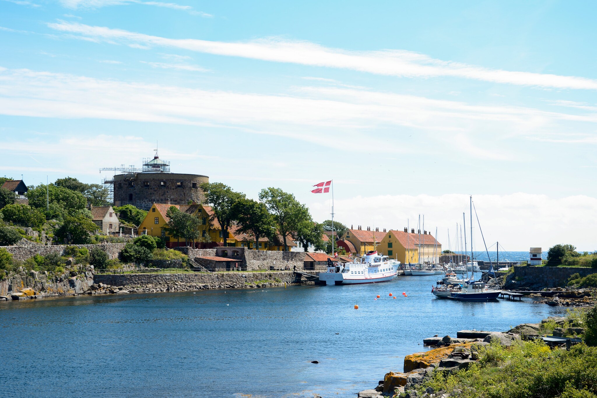 Hafen mit Segelbooten und Fähre, dänische Flagge weht, historische Festung und Häuser am Ufer auf Bornholm
