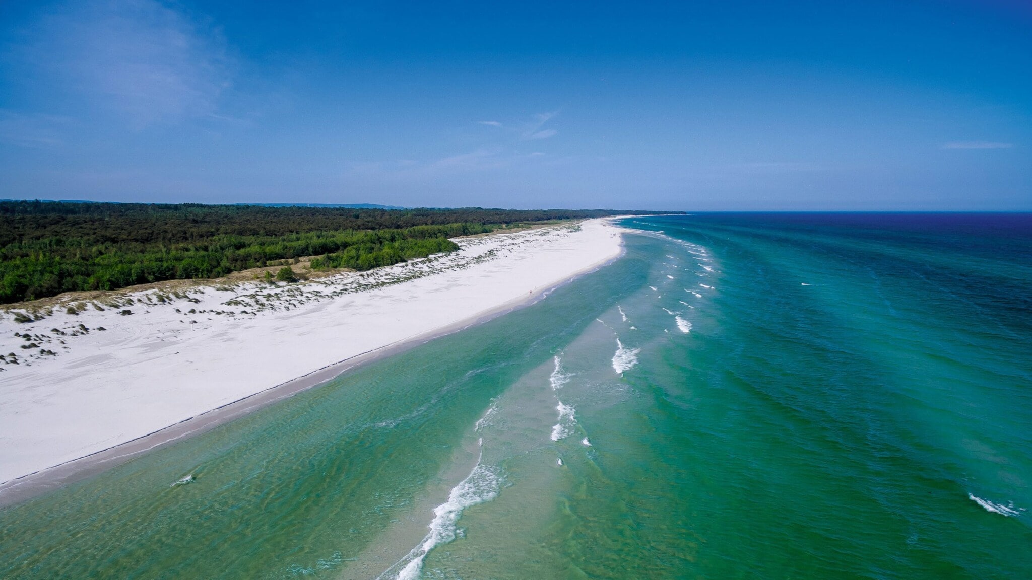 Luftaufnahme eines langen weißen Sandstrands mit grünem Wald im Hintergrund und ruhigem Meer unter blauem Himmel Luftaufnahme eines langen weißen Sandstrands mit grünem Wald im Hintergrund und ruhigem Meer unter blauem Himmel