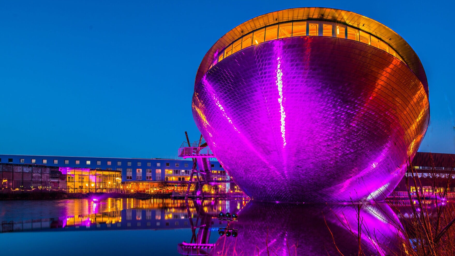 Wissenschaftsmuseum Universum Bremen in Form einer silbernen Schale, beleuchtet in Lila und Orange, am Wasser bei Nacht. Wissenschaftsmuseum Universum Bremen in Form einer silbernen Schale, beleuchtet in Lila und Orange, am Wasser bei Nacht.