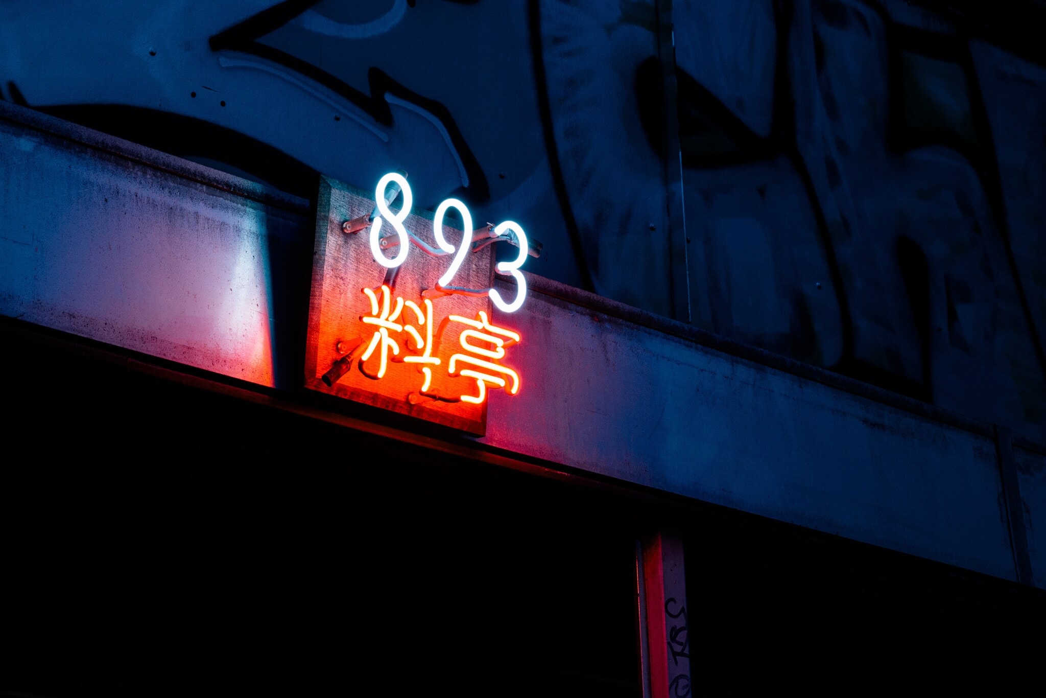 Close-up des schummrigen Neonschilds mit dem Restaurantnamen über dem unauffälligen Eingang des 893 Ryōtei. Close-up des schummrigen Neonschilds mit dem Restaurantnamen über dem unauffälligen Eingang des 893 Ryōtei.