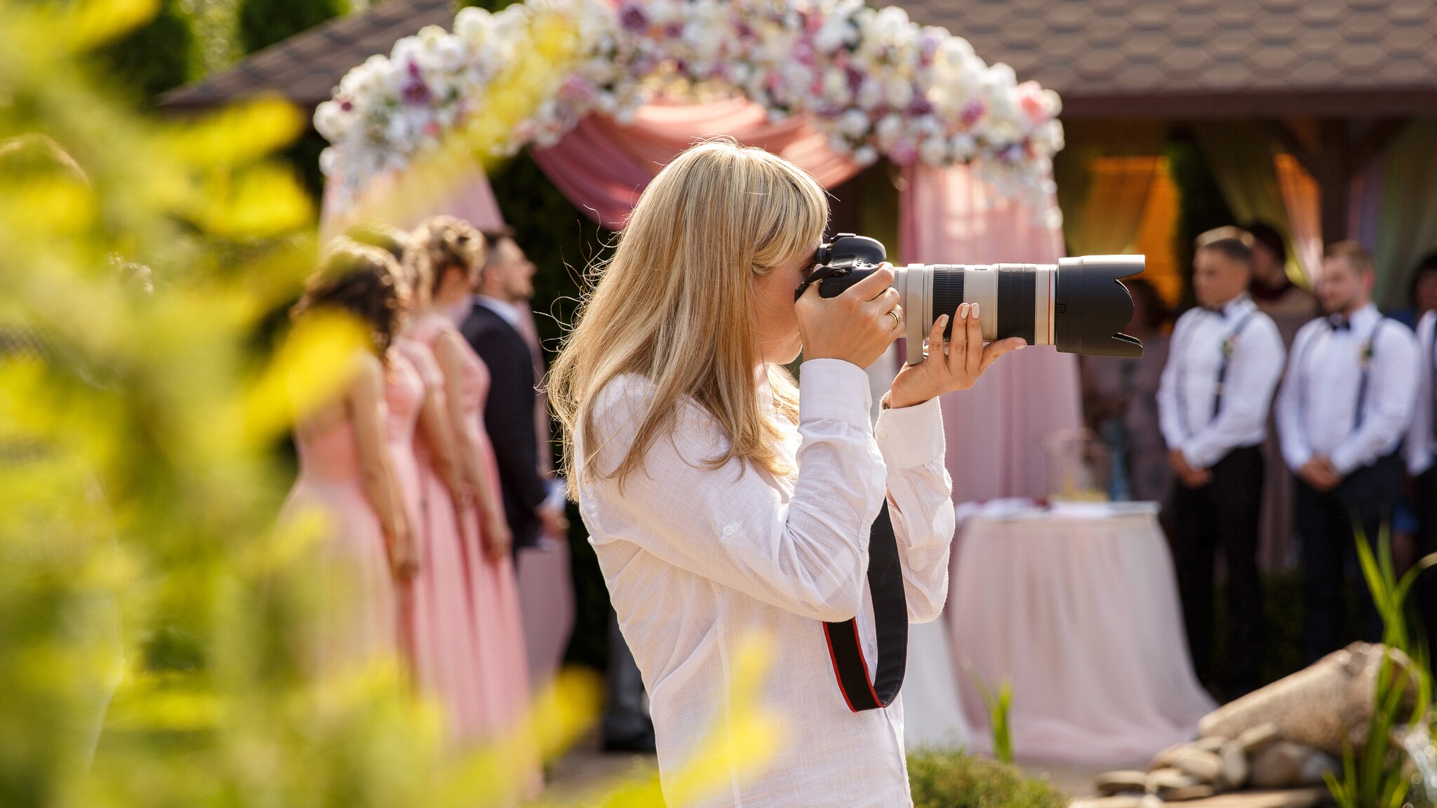 Frau mit langen blonden Haaren fotografiert mit einer Kamera mit Teleobjektiv bei einer Hochzeit im Freien.