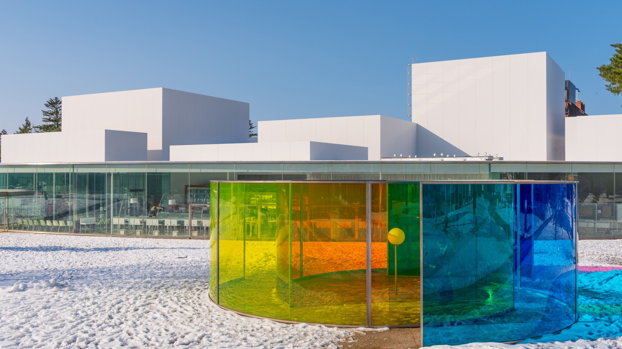 Modernes weißes Gebäude mit flachem Dach hinter einem kreisförmigen Pavillon aus farbigem Glas im Schnee Modernes weißes Gebäude mit flachem Dach hinter einem kreisförmigen Pavillon aus farbigem Glas im Schnee