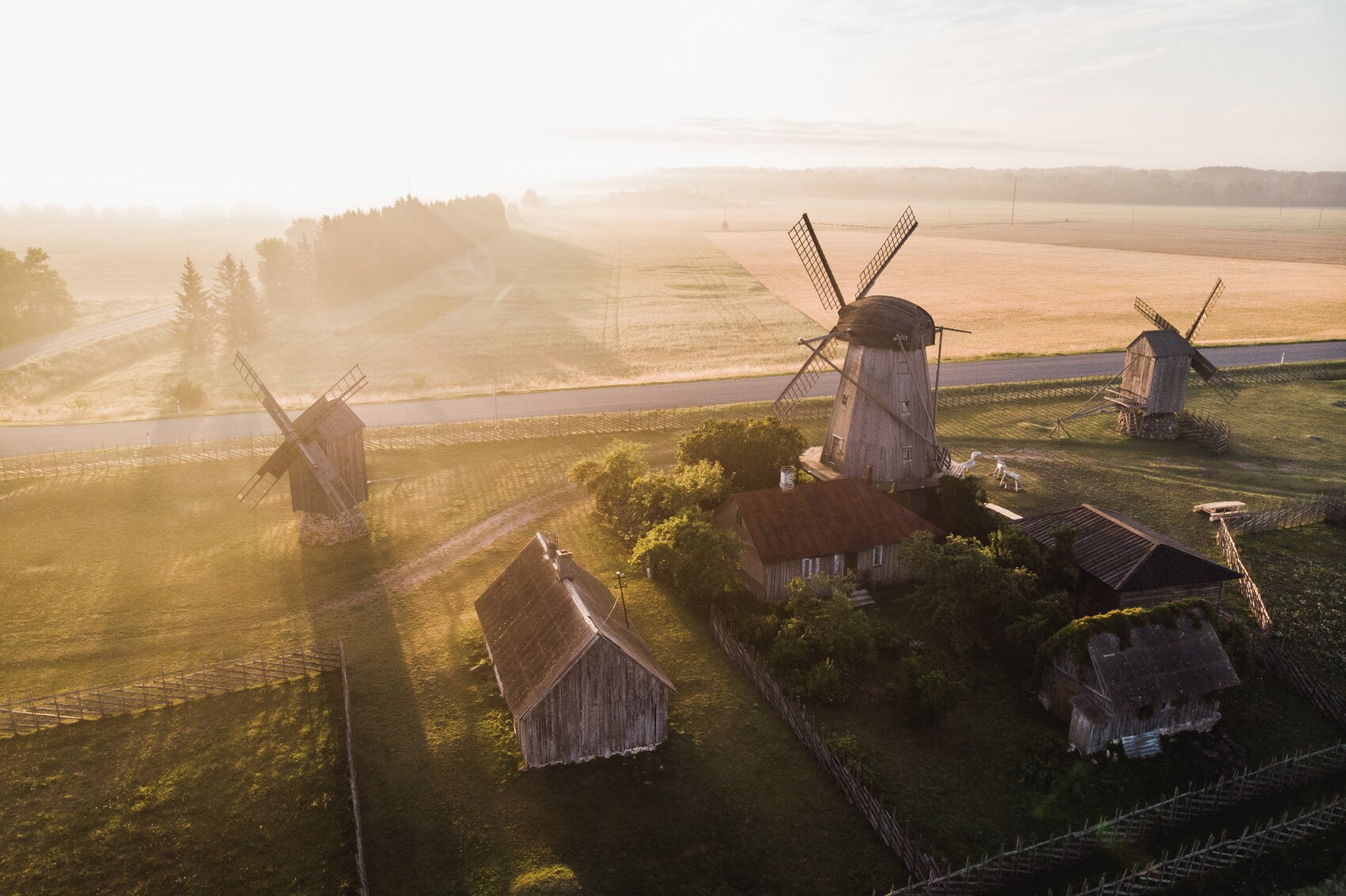 Ein ländliches Gebiet mit drei Windmühlen, Häusern und viel Grün im Sonnenschein.