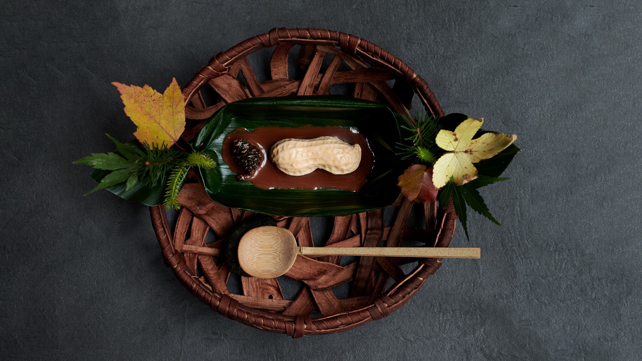 Braune Erdnuss-förmige Süßigkeit auf grünem Blatt, dekoriert mit Herbstblättern auf rundem Holztablett mit Holzlöffel