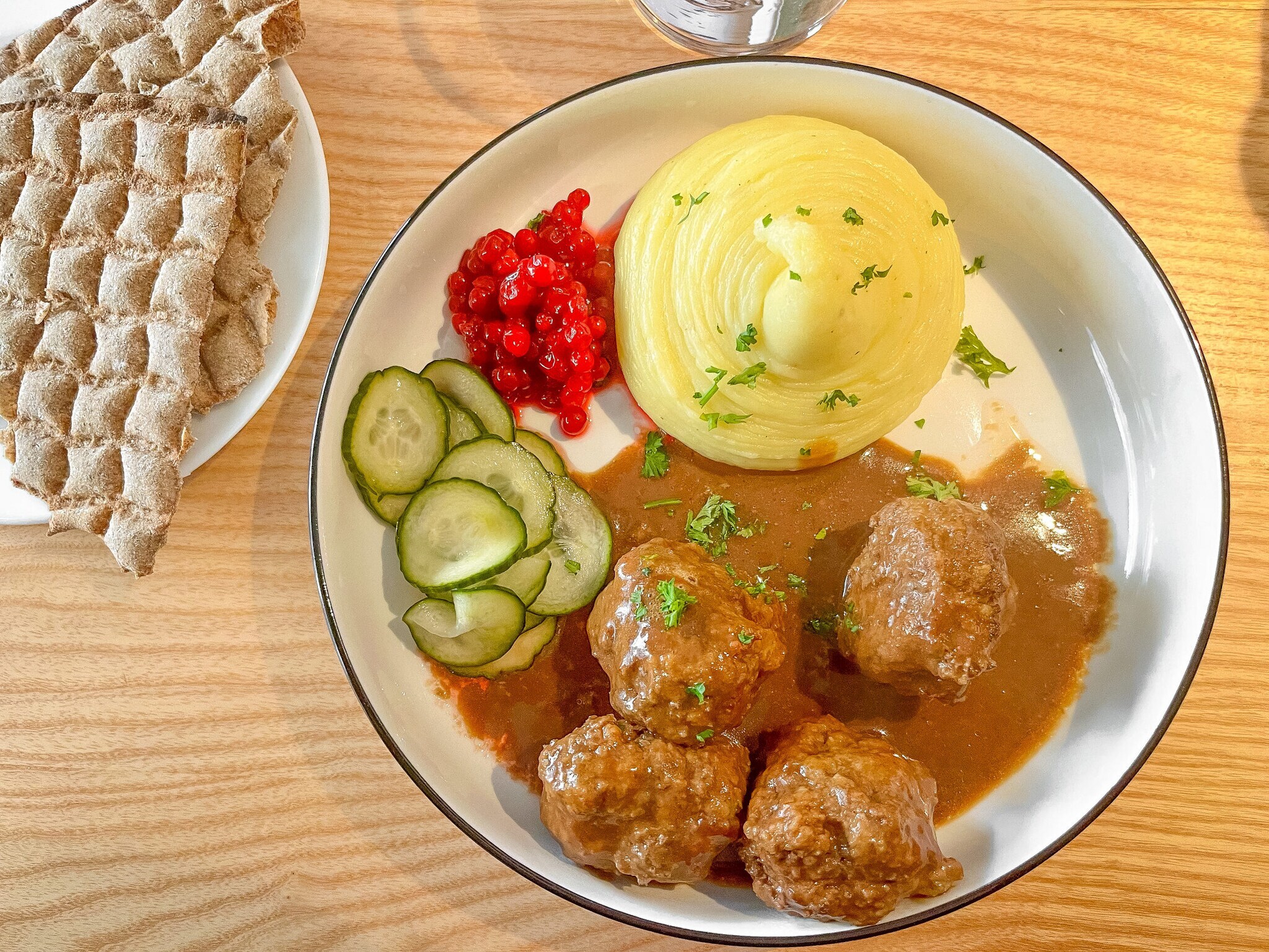 Ein Teller mit schwedischen Köttbullar, Kartoffelbrei, Gurkensalat und Preiselbeeren auf einer Holzplatte. Ein Teller mit schwedischen Köttbullar, Kartoffelbrei, Gurkensalat und Preiselbeeren auf einer Holzplatte.