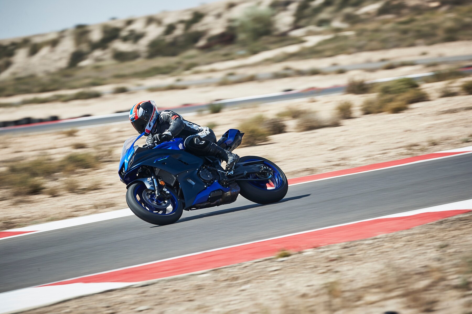 Eine blaues Motorrad vom Typ Yamaha R7 fährt über eine Rennstrecke mit rot-weißen Fahrbahnmarkierungen Eine blaues Motorrad vom Typ Yamaha R7 fährt über eine Rennstrecke mit rot-weißen Fahrbahnmarkierungen