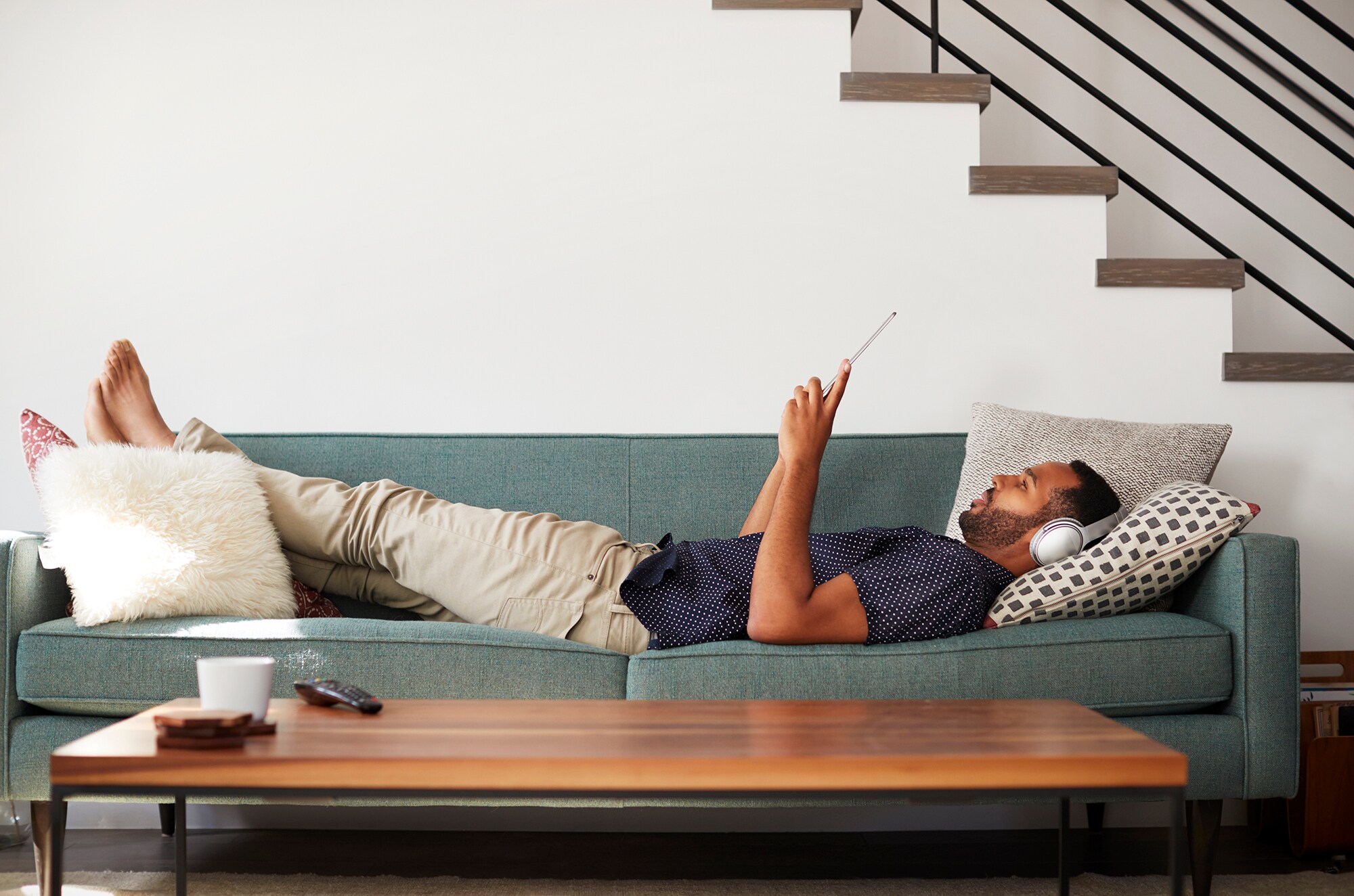 Mentale Gesundheit für Selbstständige: So behältst du die Balance im stressigen Business-Alltag Ein Mann liegt mit Kopfhörern über den Ohren auf einem Sofa und liest.