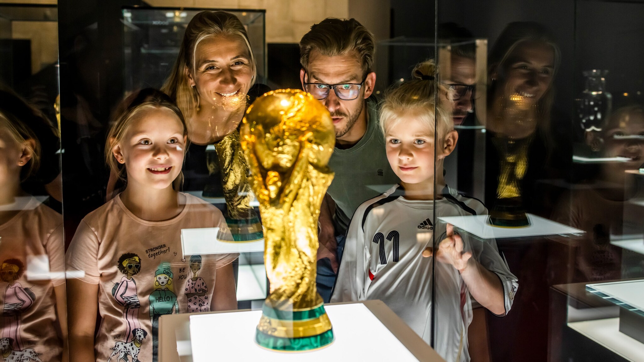 Eltern mit Kindern stehen um den FIFA-Weltmeisterschaftspokal in einer Vitrine im Museum Schatzkammer