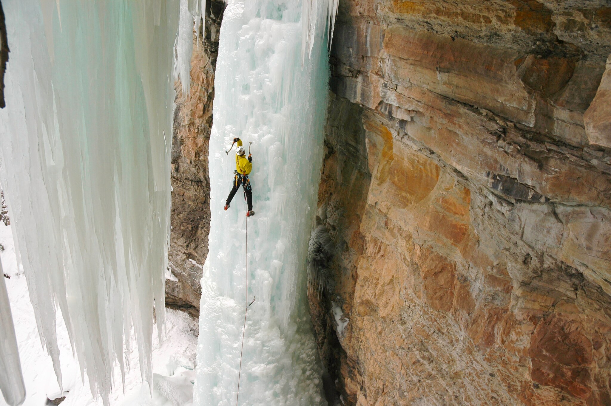 Eine Person klettert mit einem Seil gesichert einen gefrorenen Wasserfall hinauf. Eine Person klettert mit einem Seil gesichert einen gefrorenen Wasserfall hinauf.