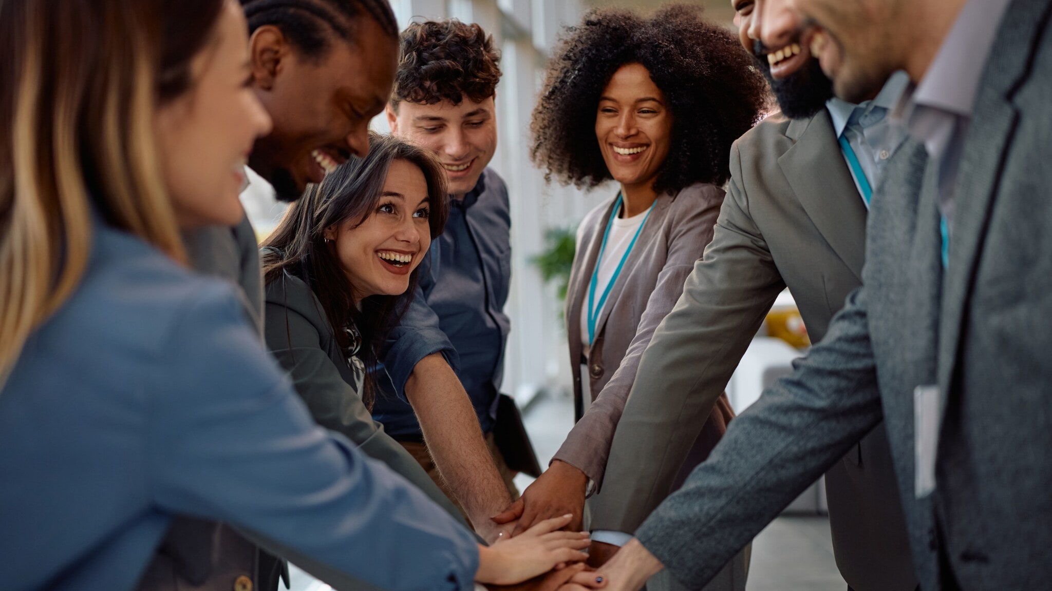 Sieben lächelnde Personen in Business-Kleidung stehen im Kreis und legen die Hände übereinander. Sieben lächelnde Personen in Business-Kleidung stehen im Kreis und legen die Hände übereinander.