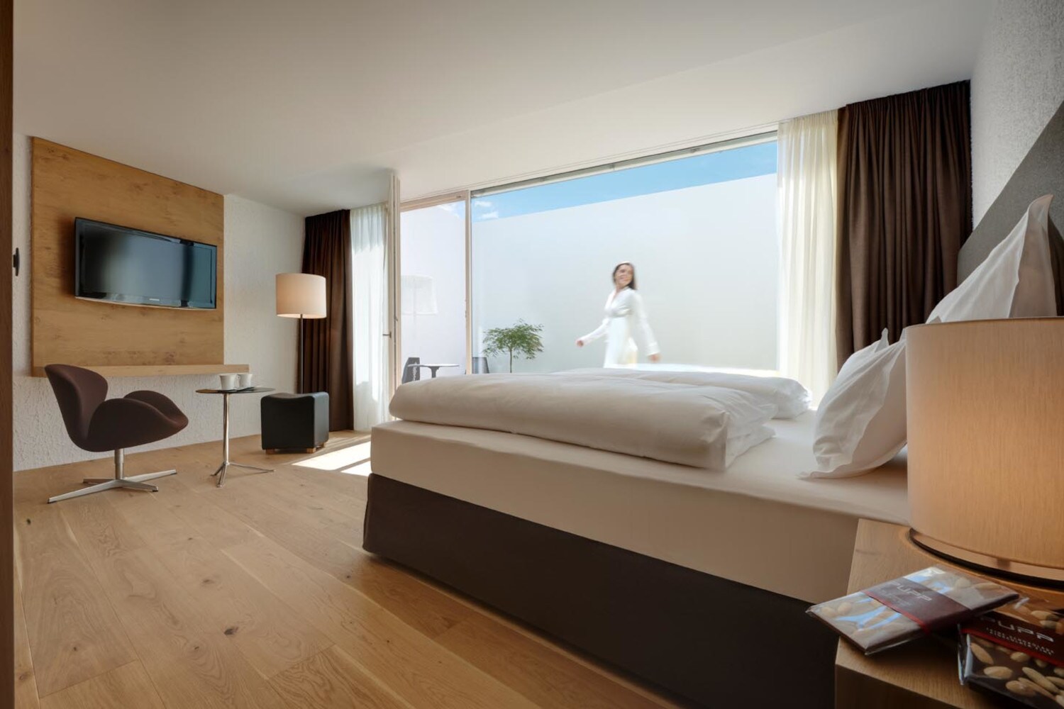 Ein Hotelbett steht vor einem großformatigen Fenster Ein Hotelbett steht vor einem großformatigen Fenster