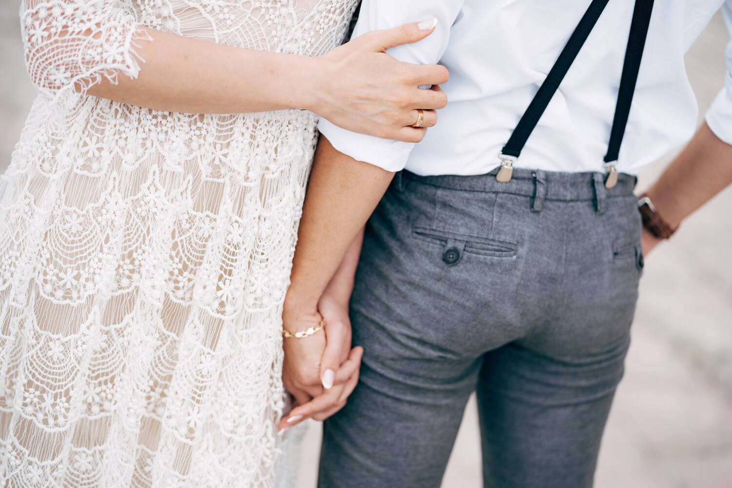 Eine Braut hält die Hand ihres Bräutigams, der Hosenträger trägt.