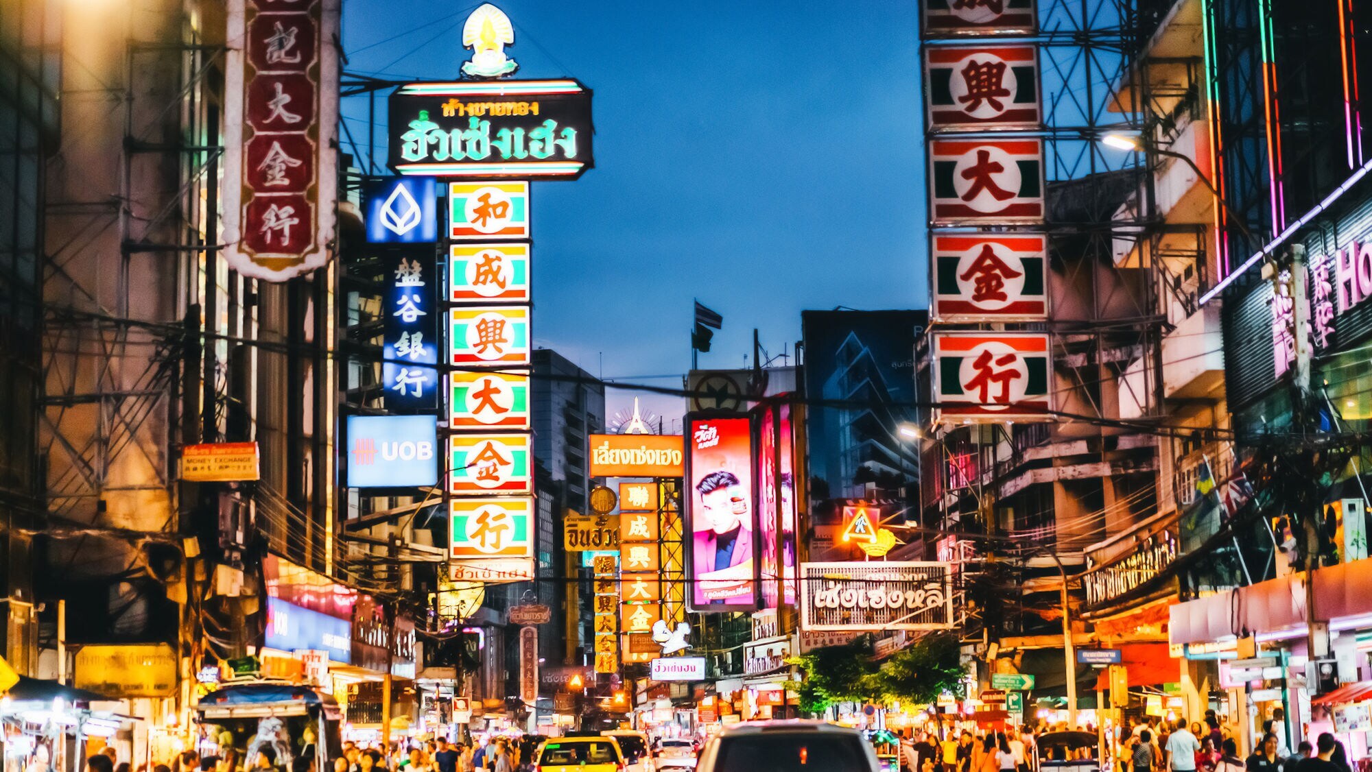An Häusern hängen viele bunte und auffällige Leuchtreklamen, die Straßen sind voll mit Spaziergängern und Autos.