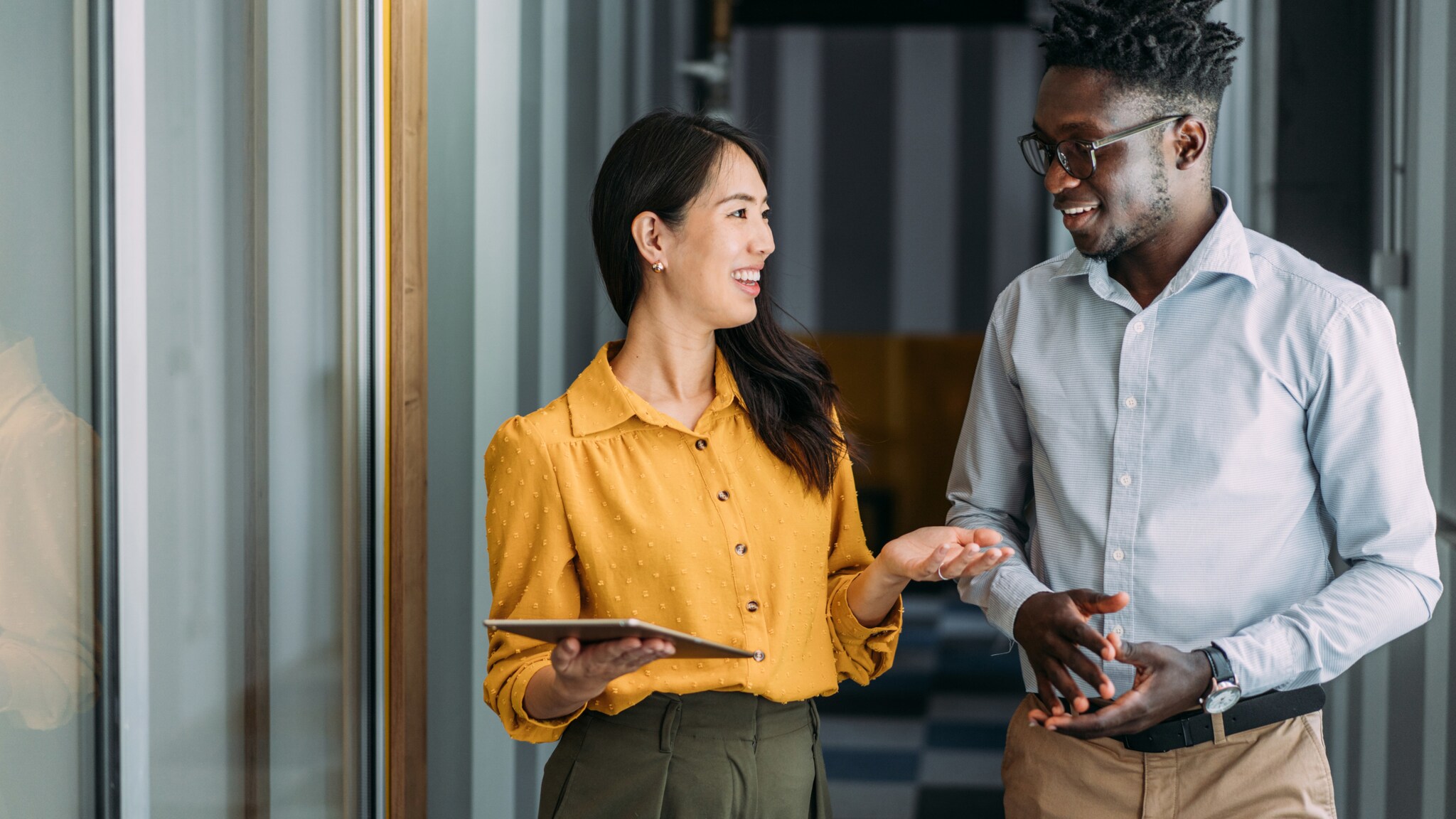 Eine Frau und ein Mann in Business-Kleidung kommunizieren freundlich in einem Flur.