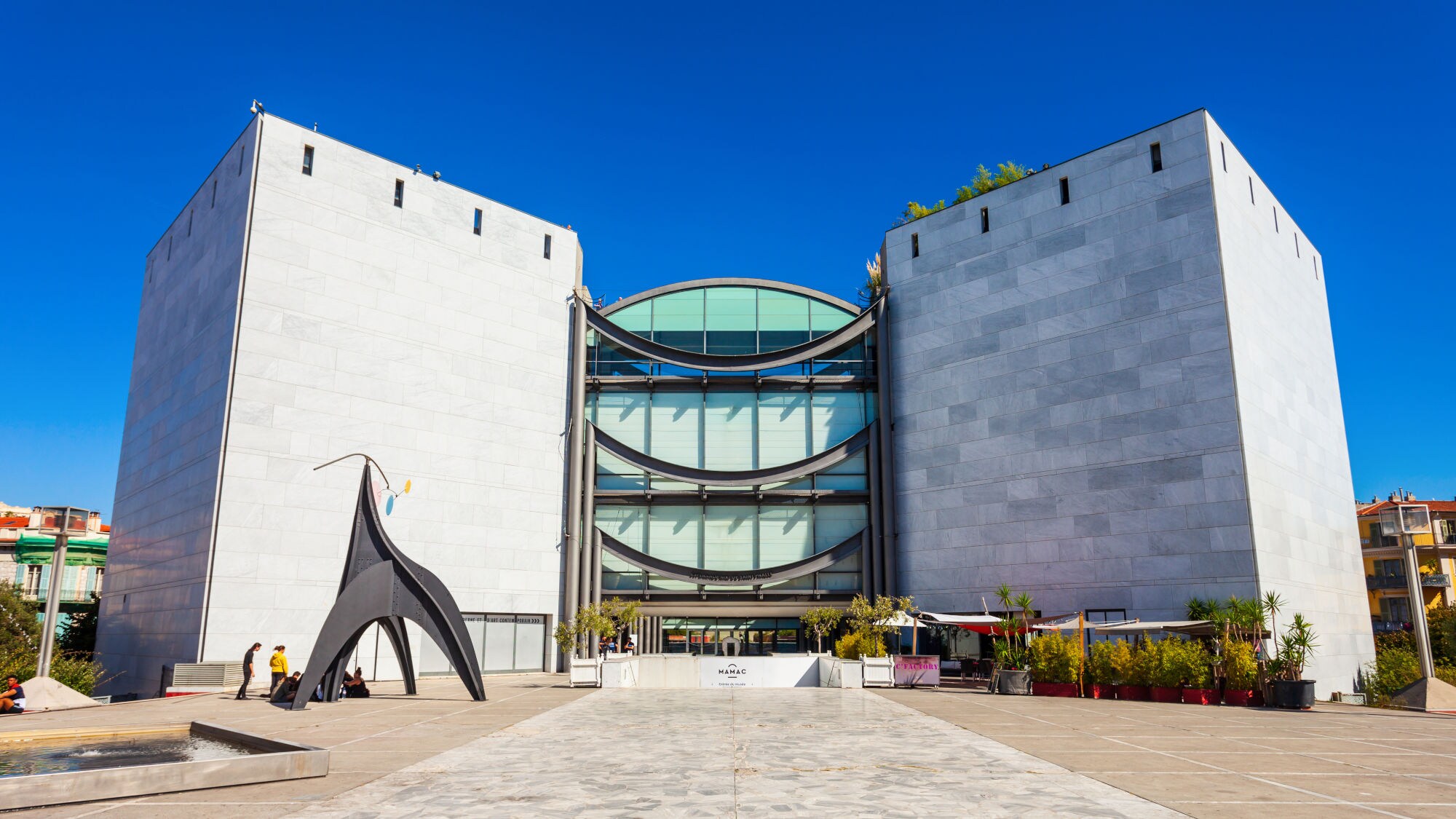 Moderne Architektur eines Gebäudes mit zwei großen, rechteckigen Türmen aus hellem Stein. Vor dem Gebäude steht eine schwarze Skulptur. Klare blaue Himmel.